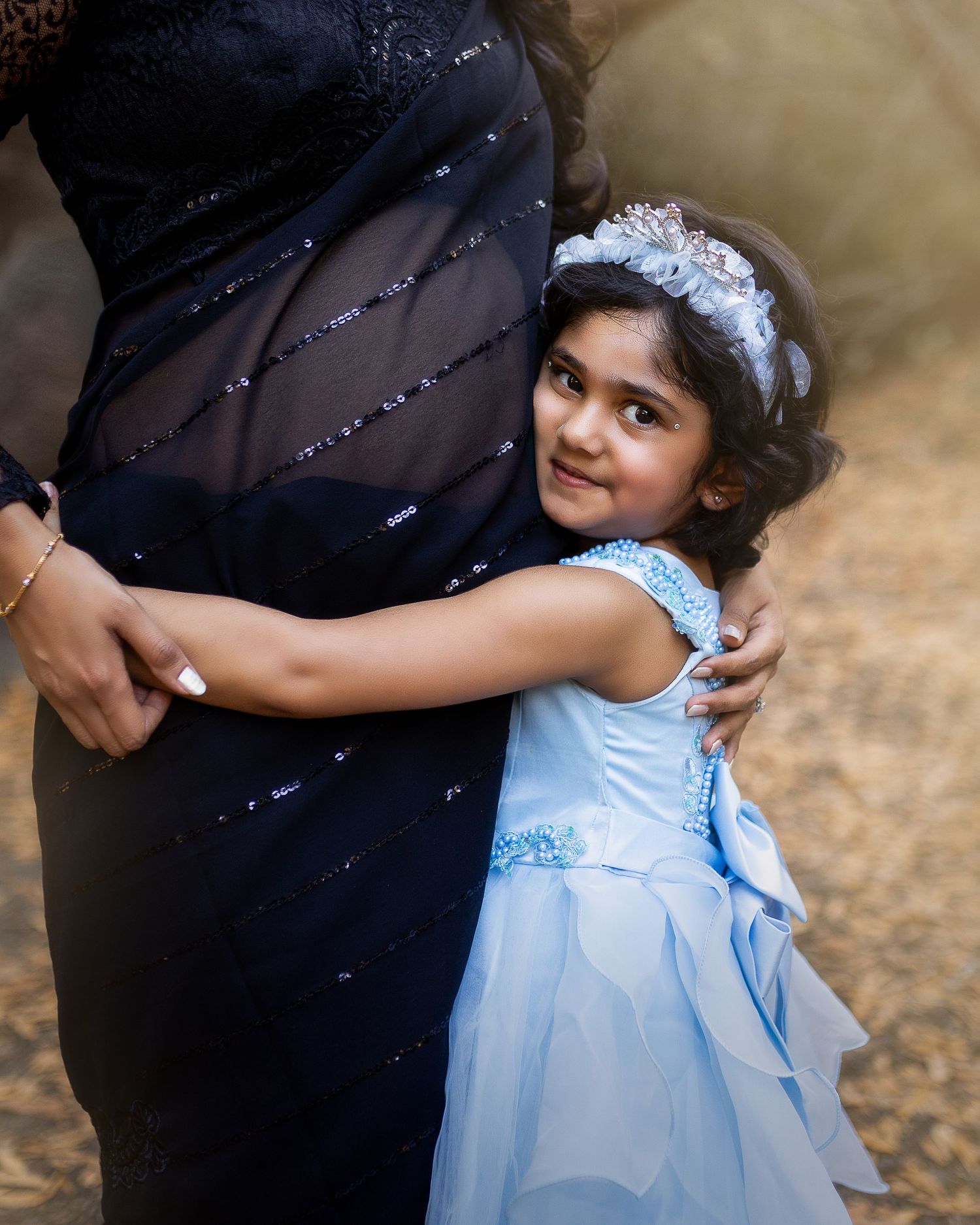 A small child in a light blue dress hugs someone wearing black clothing while standing outdoors.