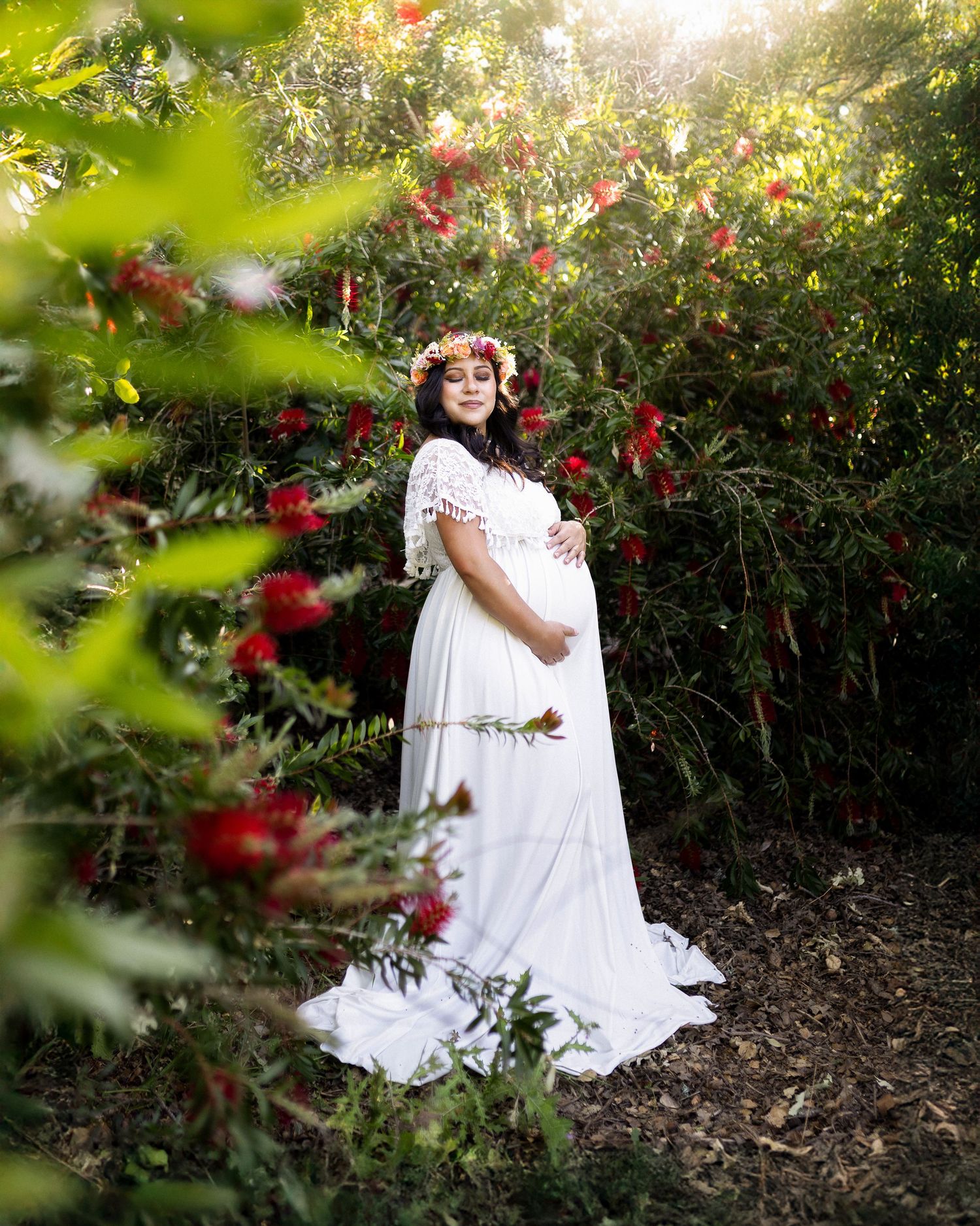 A white-dressed figure sits among lush greenery and red roses in a dreamy garden setting.