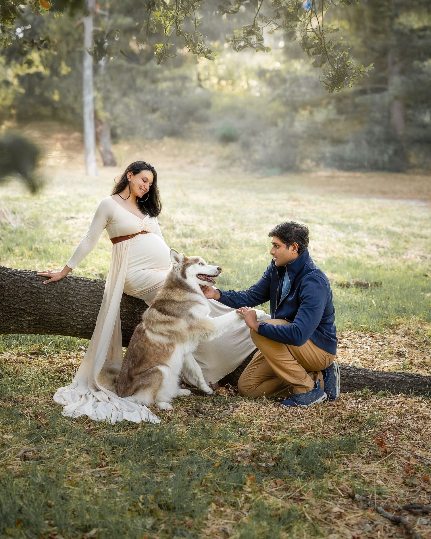 A couple sits together with their dog on fallen autumn leaves in a romantic outdoor photoshoot.