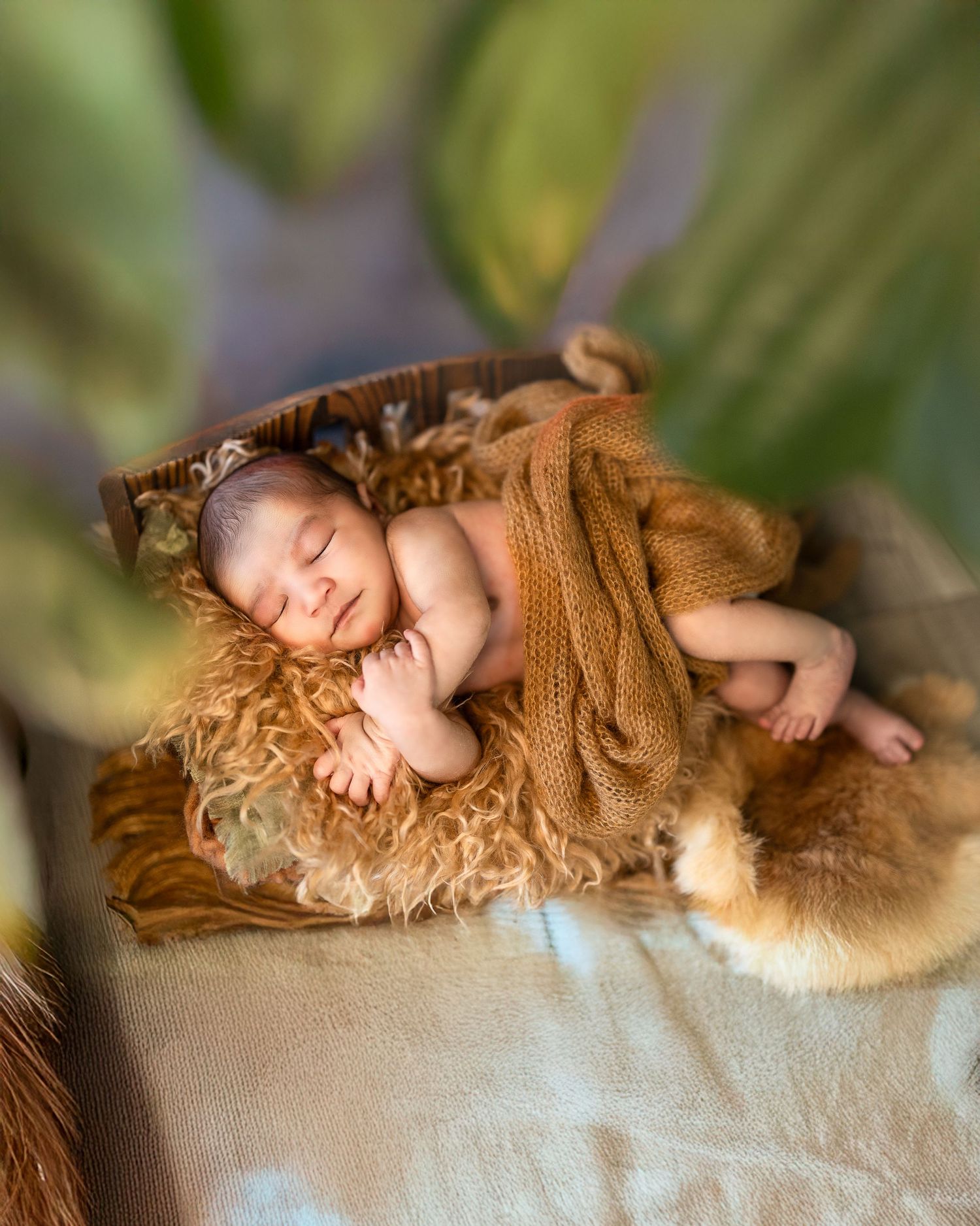 A sleeping newborn wrapped in a brown blanket lies peacefully on a soft furry surface in a dreamy nature-inspired setting.