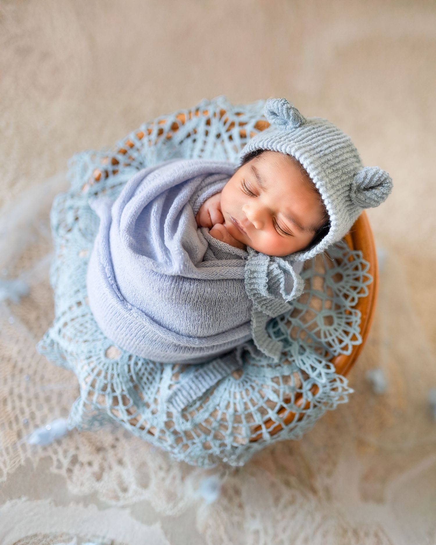 A sleeping baby wearing a soft gray knit outfit rests peacefully on a delicate lace doily.