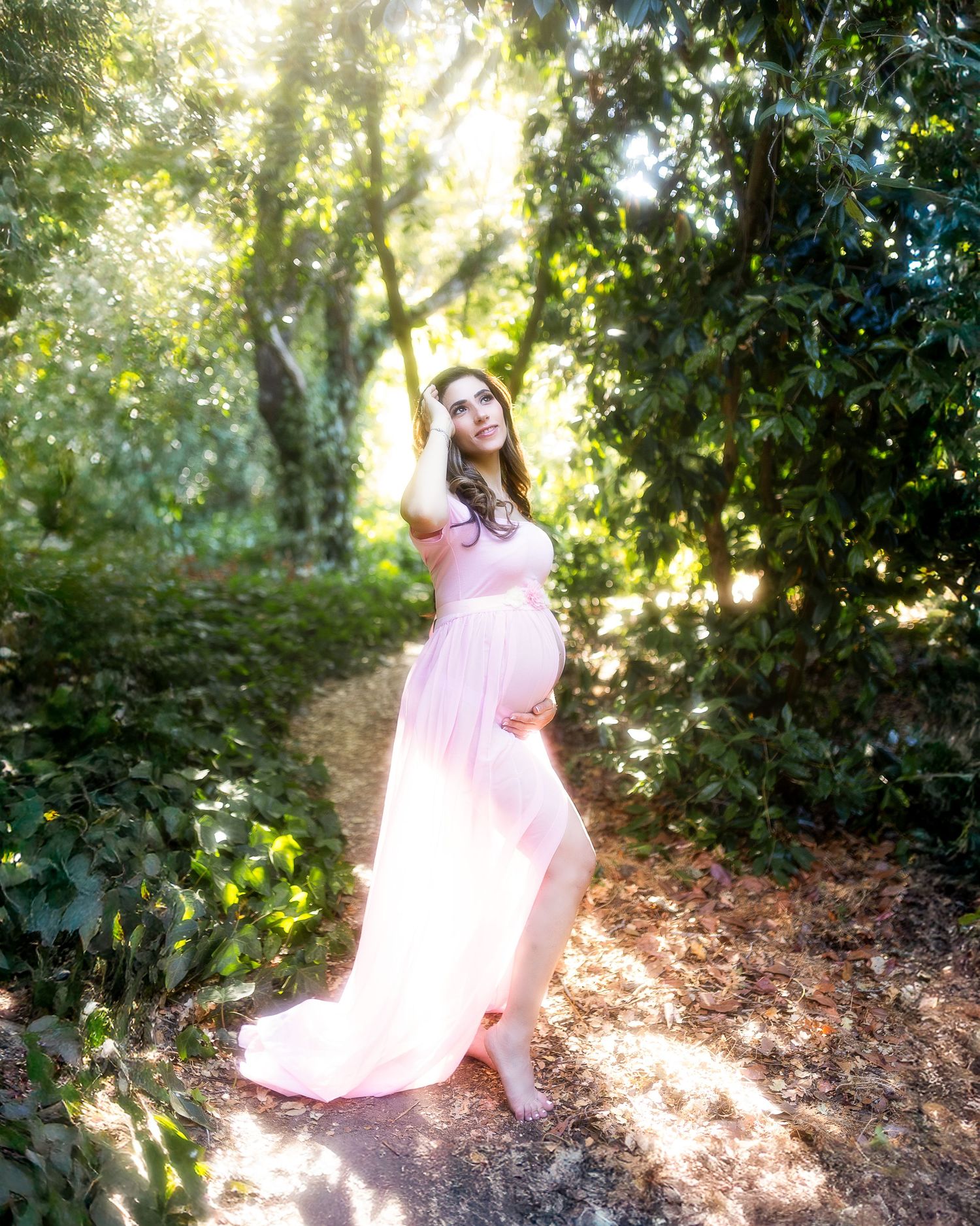A person in a flowing pink dress twirls gracefully in a sunlit wooded area creating a dreamy ethereal scene.