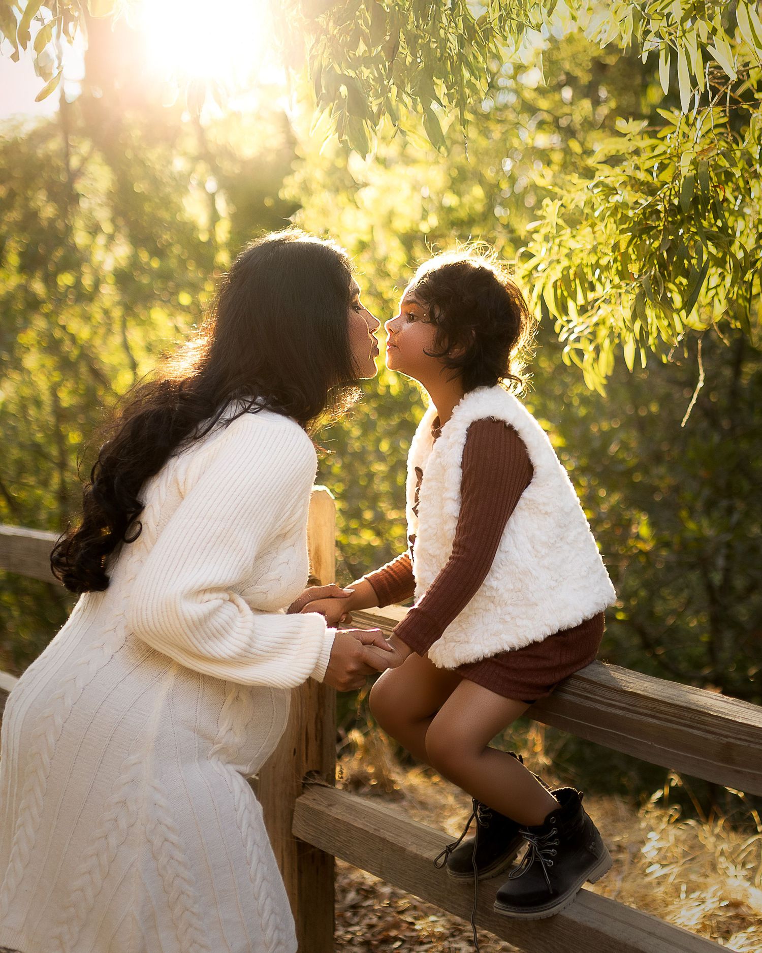 Two people share a tender moment on a wooden bench surrounded by sunlit foliage in a romantic outdoor setting.