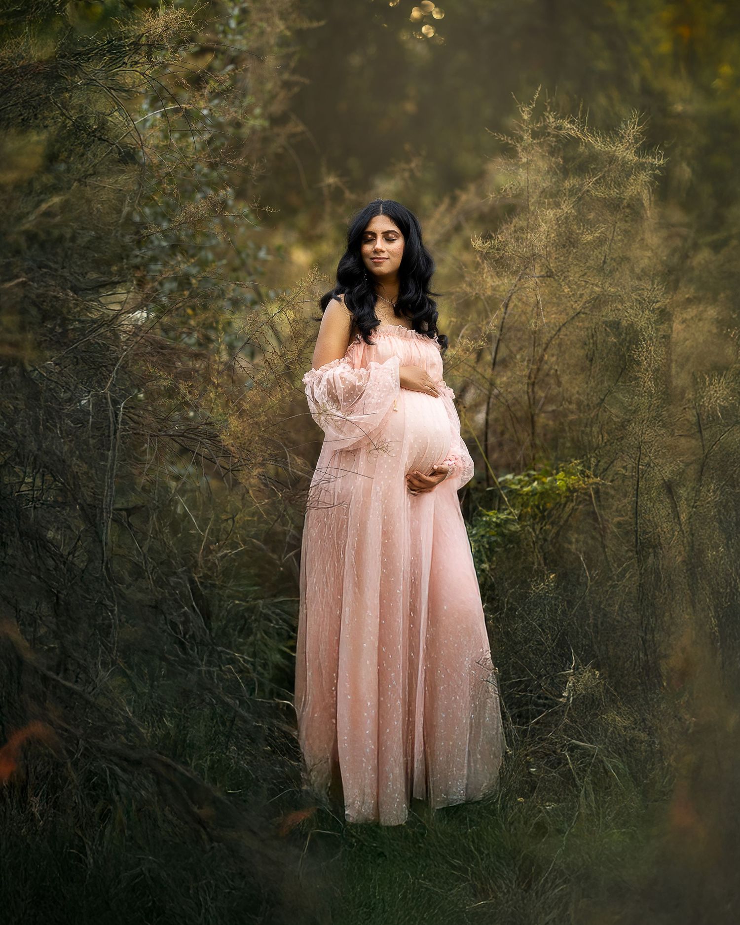 A person in a flowing pink tulle dress poses gracefully in a dreamy forest setting during golden hour.