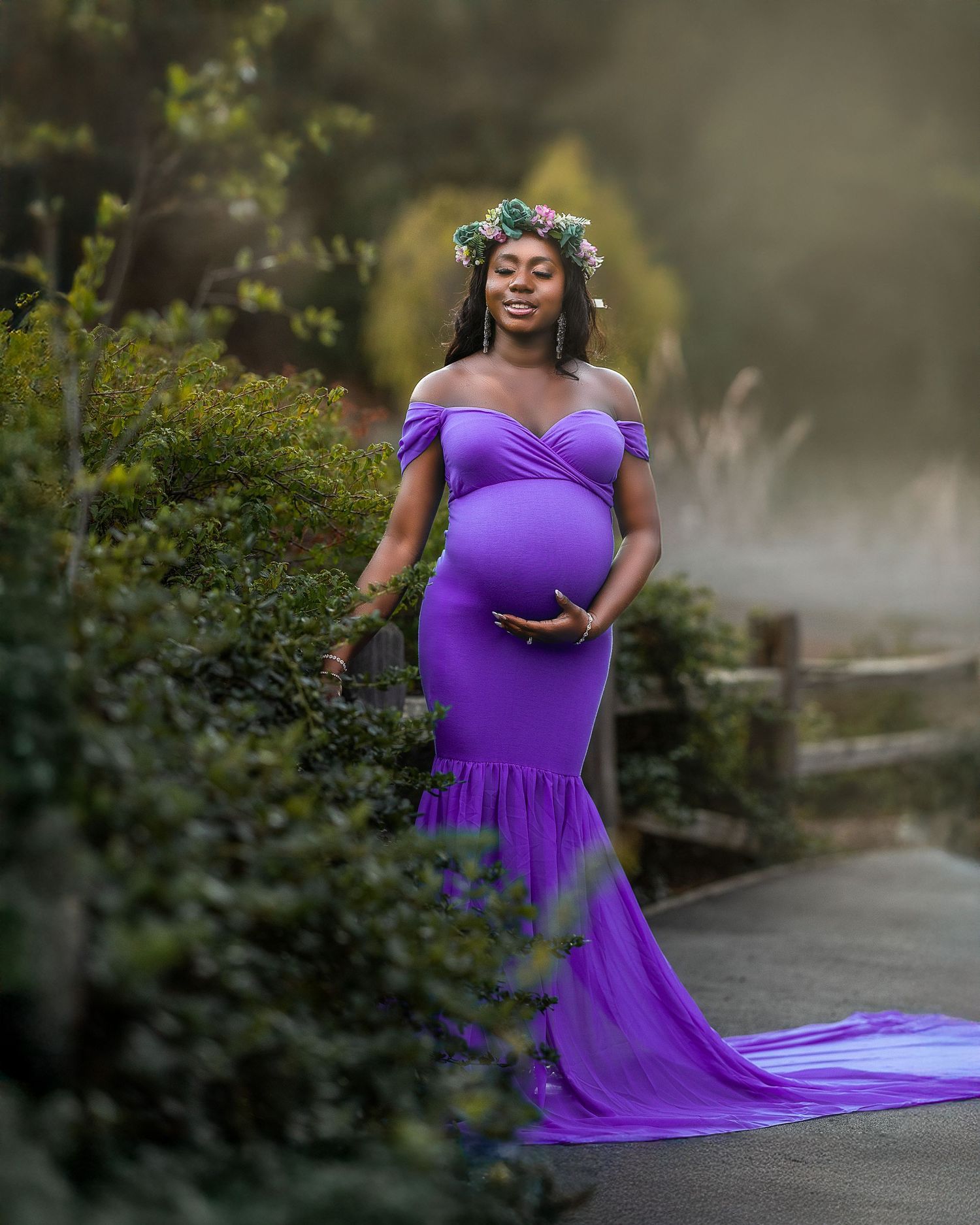 A person in a flowing purple gown poses gracefully in an outdoor garden setting during a photo session.