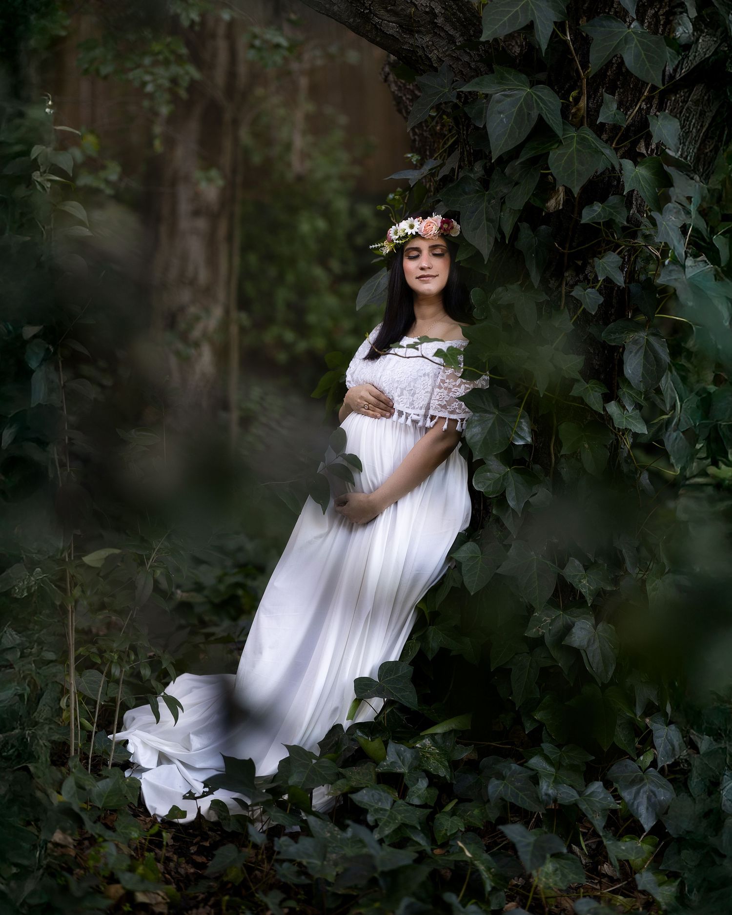 Ethereal figure in flowing white dress poses mysteriously among dark foliage in a moody forest setting.