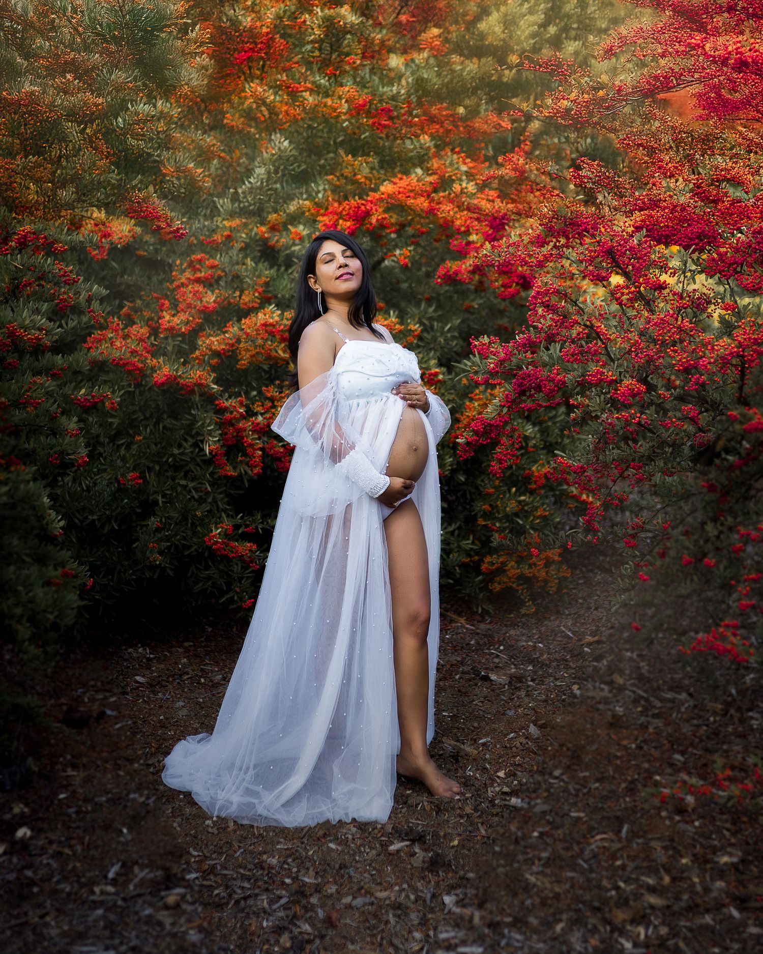A flowing white dress contrasts beautifully against vibrant red and orange autumn foliage in a romantic outdoor portrait.