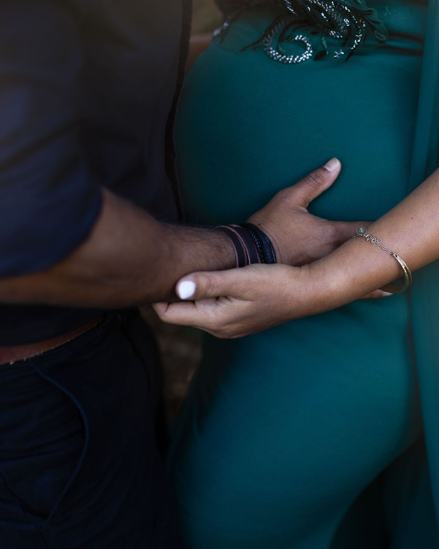 Close-up series showing hands gently cradling a pregnant belly in teal maternity dress against dark background.