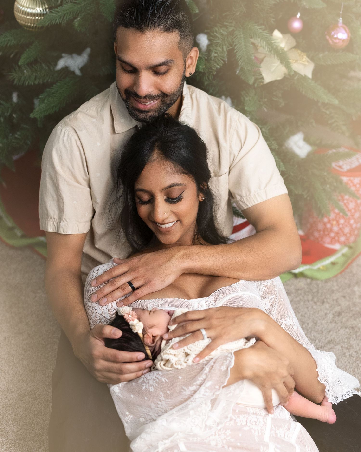 A couple in light colored outfits share a tender moment while looking at a phone against a festive holiday backdrop.