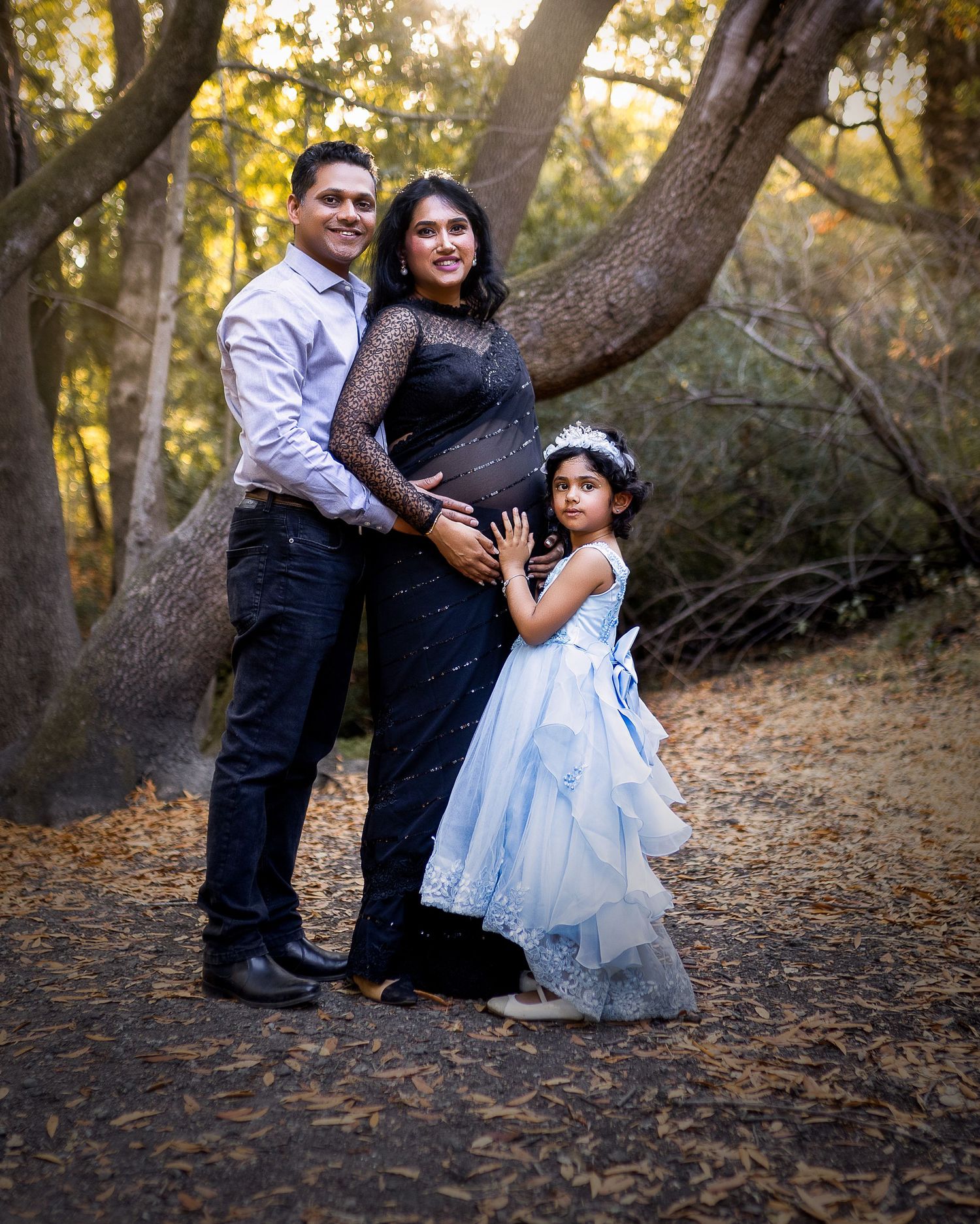 Family photo session in a wooded area during golden hour with warm autumn lighting and natural scenery.
