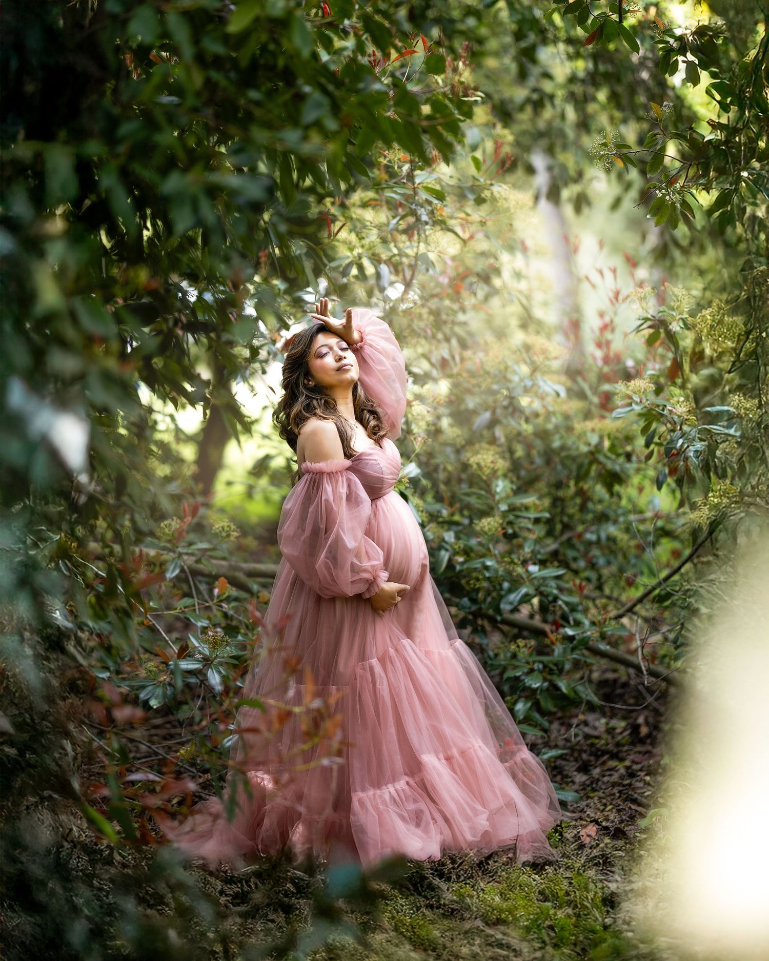A mother and child in matching pink tulle dresses share tender moments in a sunlit garden setting.