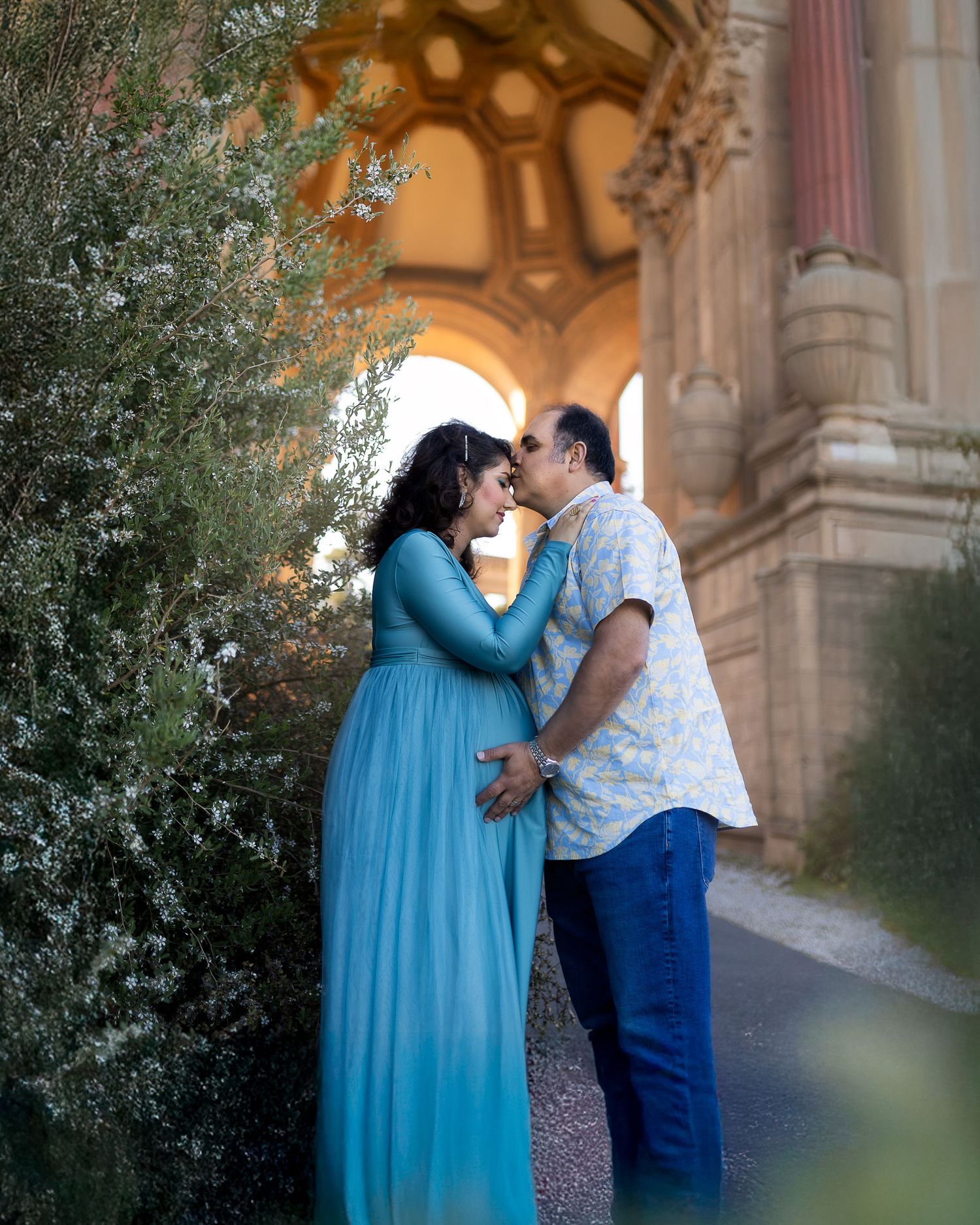 A romantic couple shares a tender moment under an ornate archway at sunset.