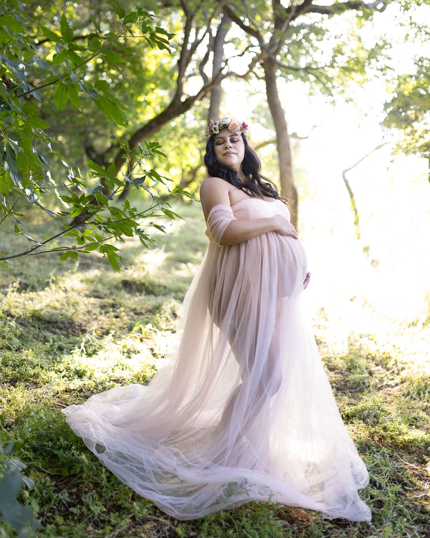 A flowing blush pink tulle gown creates an ethereal scene in a sunlit woodland setting.