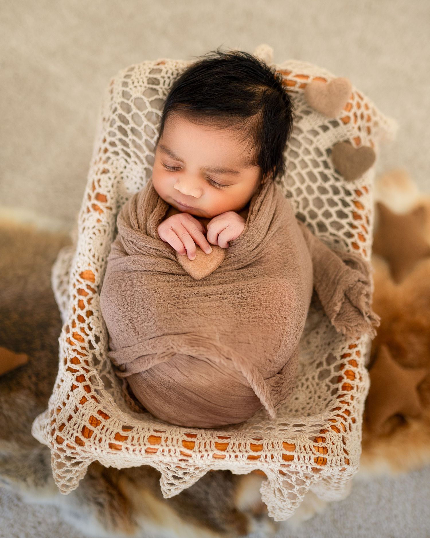 Artistic overhead portrait of a sleeping baby nestled in brown swaddle on cream lace backdrop.
