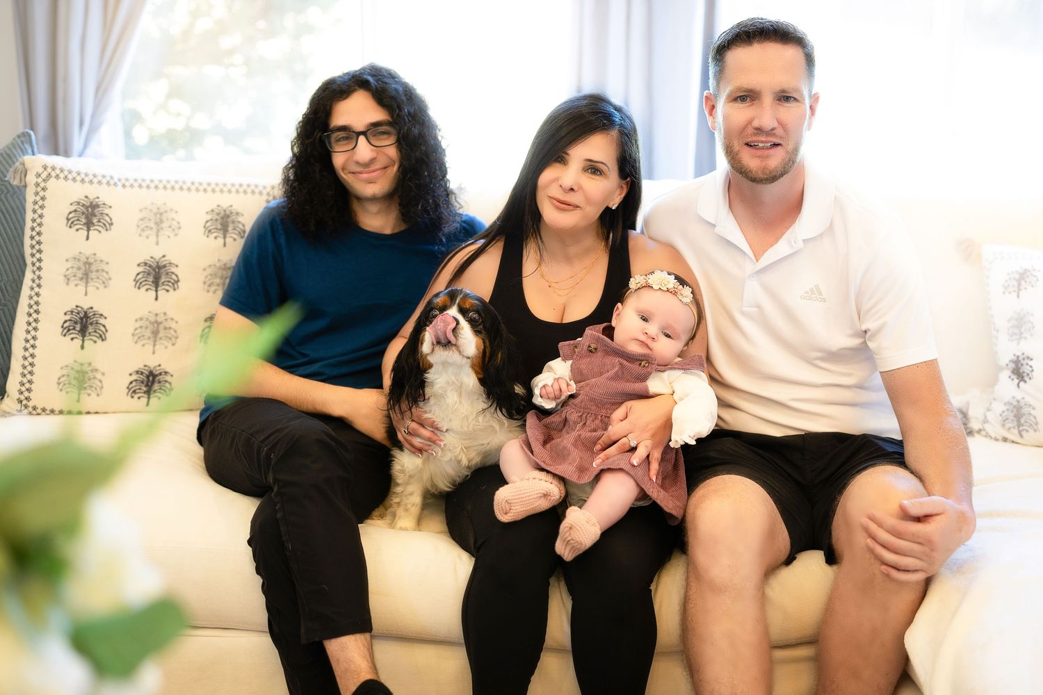 A group of people sit together on a white couch in a living room setting.