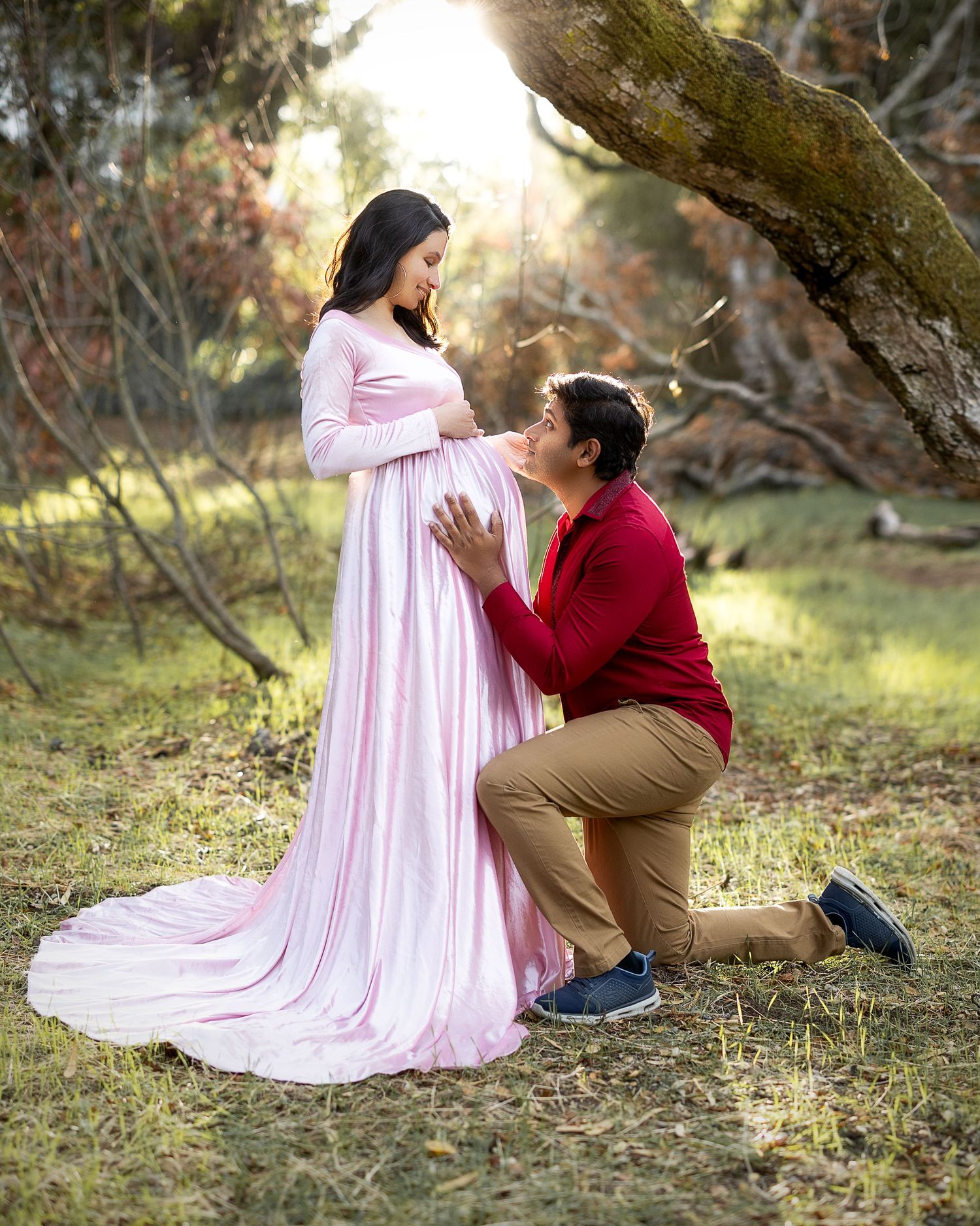 A couple shares a tender moment outdoors in autumn, with one person wearing a flowing pink dress and another in burgundy.