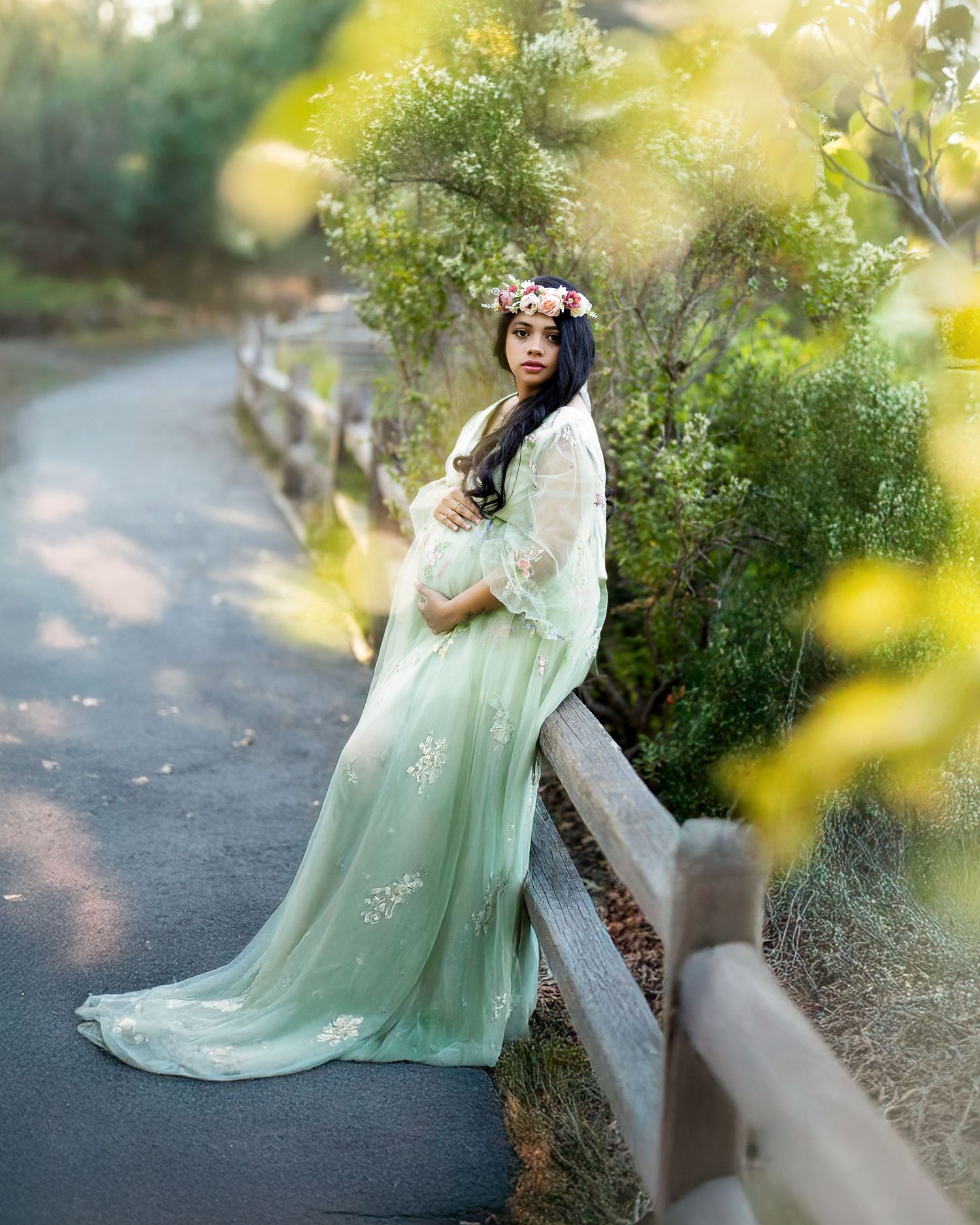A dreamy maternity photoshoot in a garden setting with soft sunlight filtering through leaves and a flowing mint green dress.