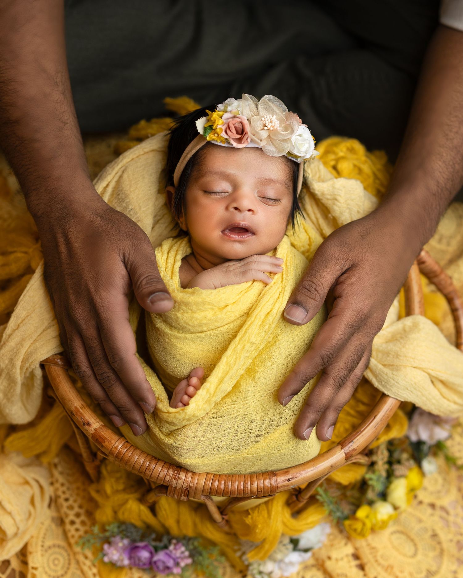 A series of images showing a newborn baby swaddled in yellow fabric being gently placed in a woven basket.