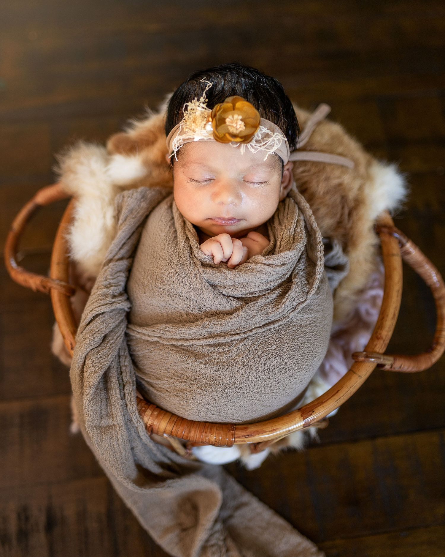 Newborn baby wrapped in gray swaddle blanket lying on wooden surface with soft lighting and rustic backdrop.