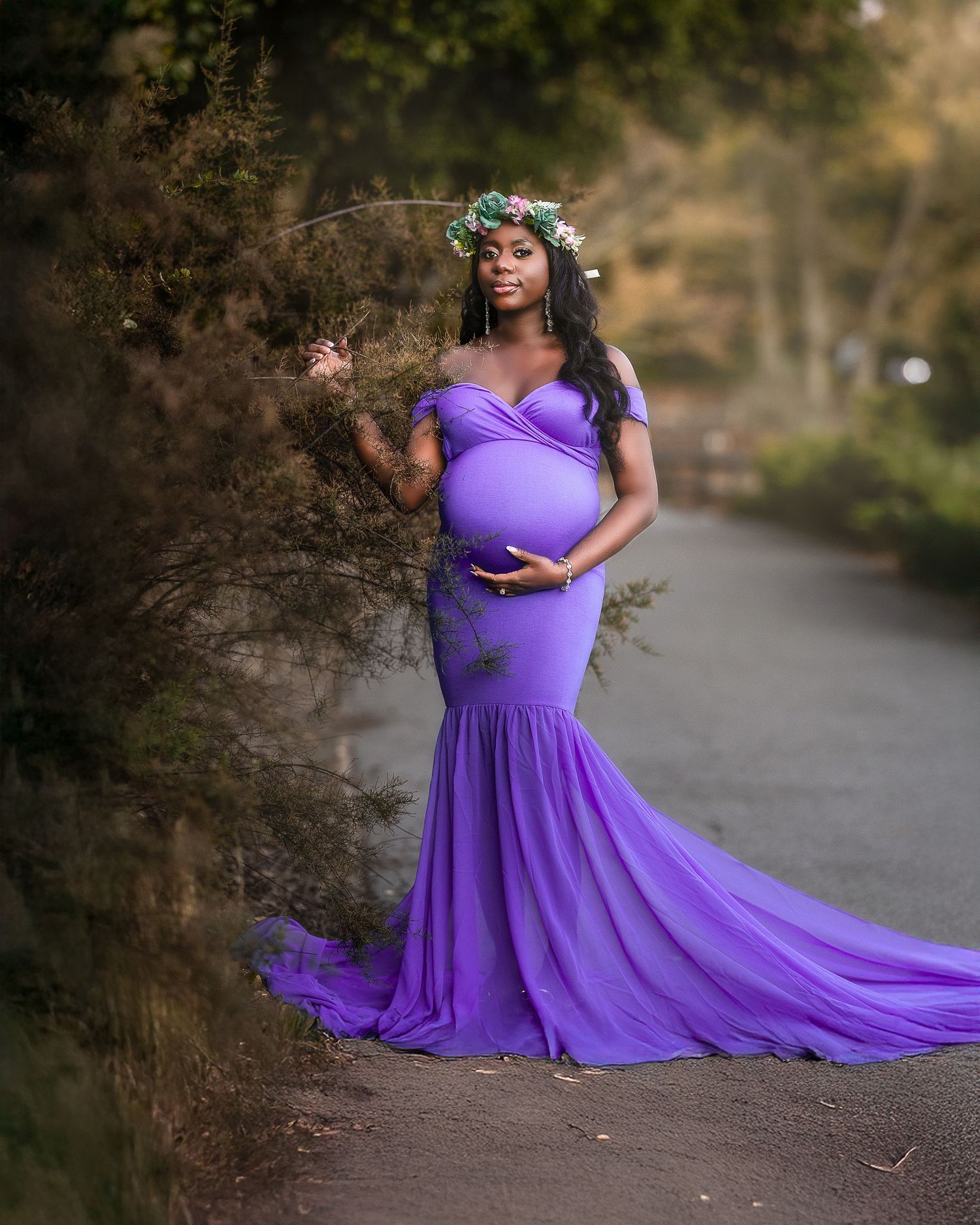 A flowing purple maternity gown billows gracefully along a wooded path during a sunset photoshoot.
