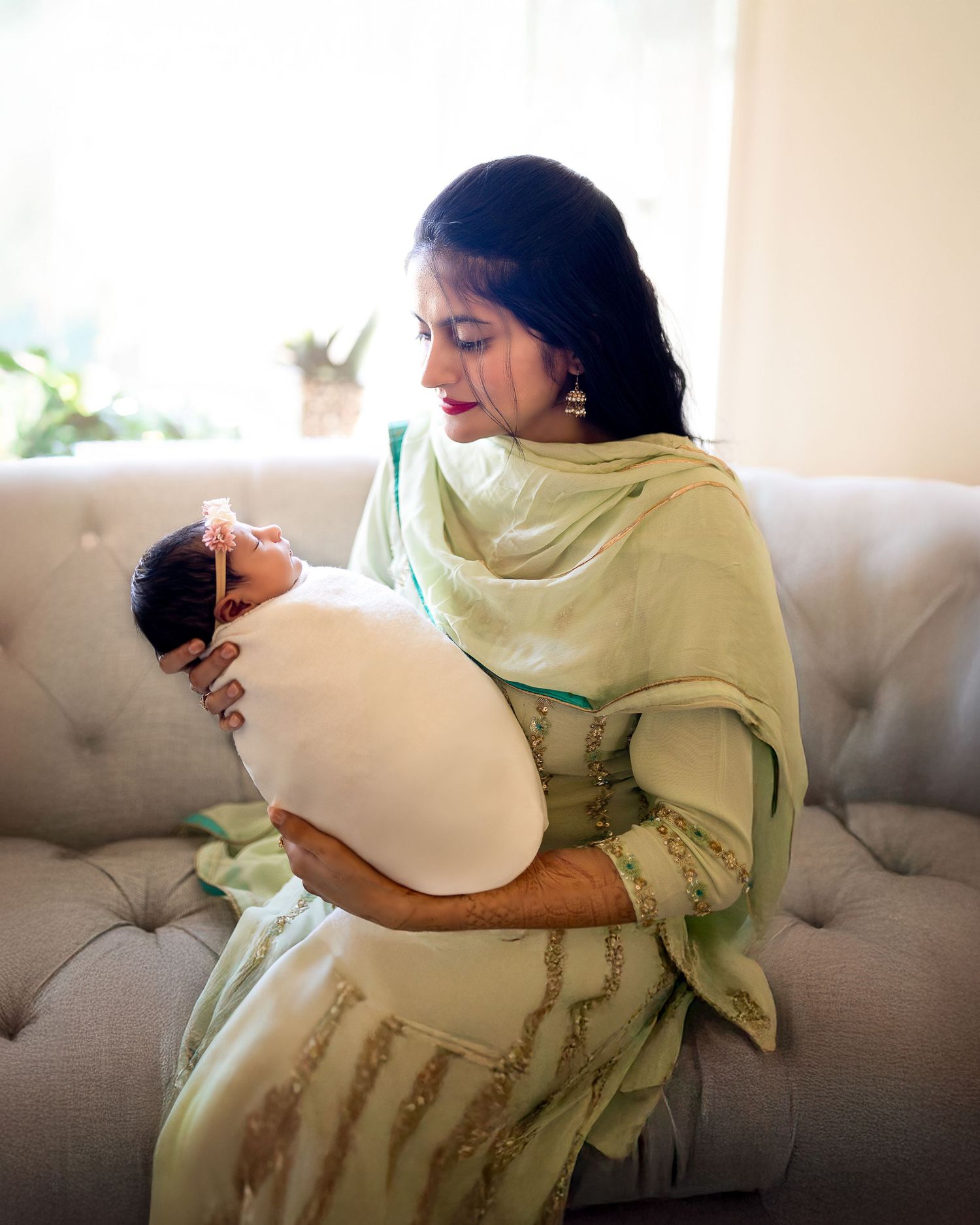 Person in light green traditional dress sitting on gray couch in sequence of relaxed poses.