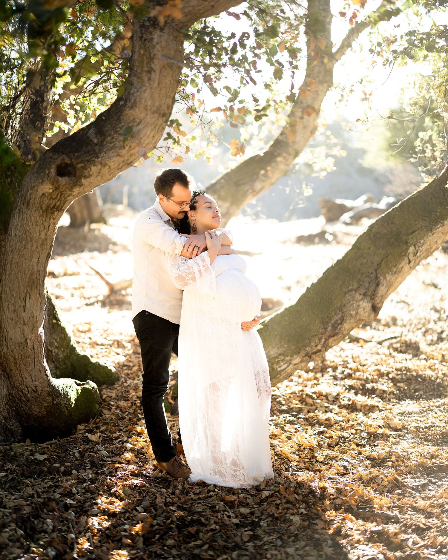 A couple in wedding attire shares romantic moments under sunlit trees in a dreamy outdoor setting.