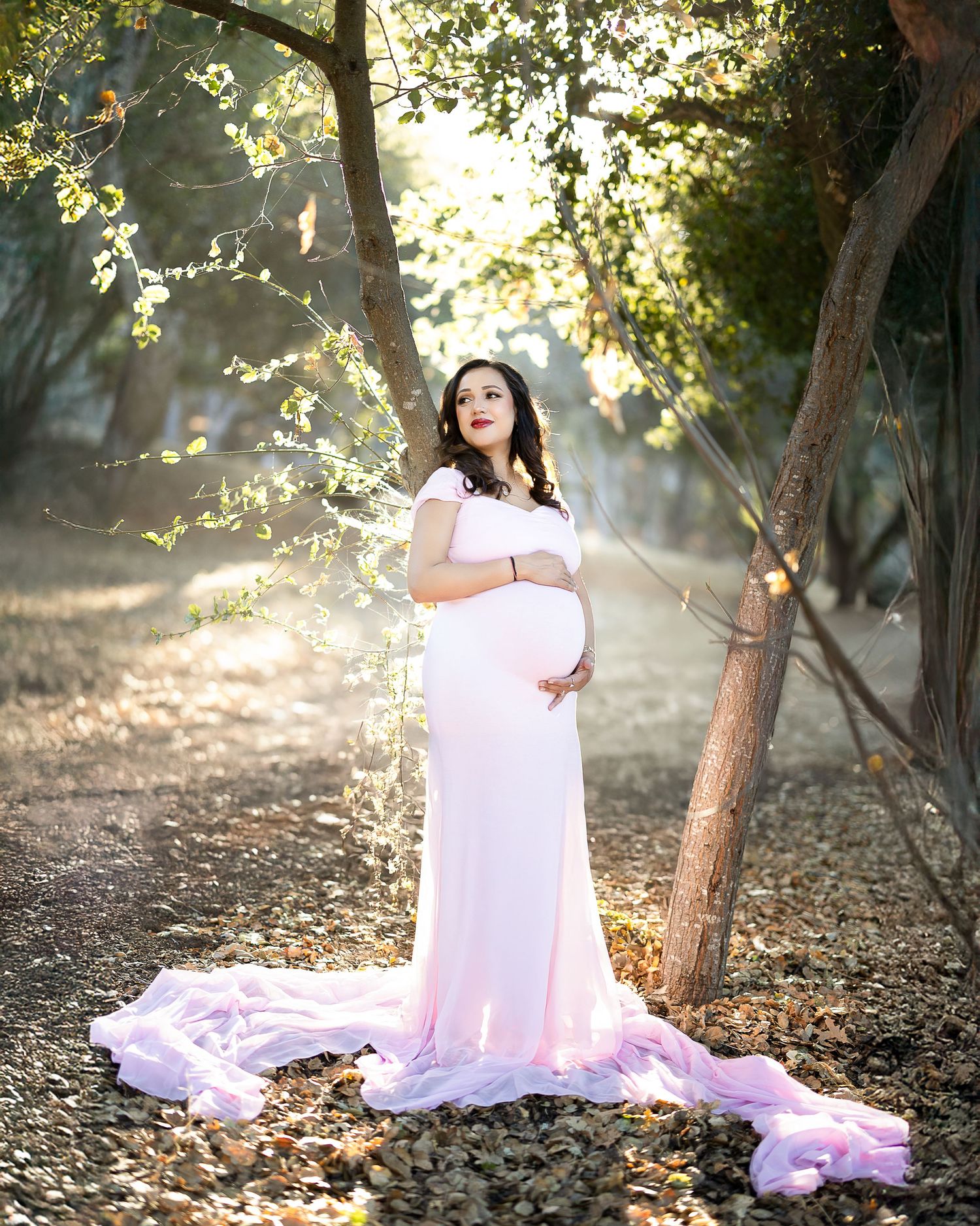 A dreamy outdoor photoshoot in a sunlit forest with soft white fabric and ethereal lighting creating a magical atmosphere.