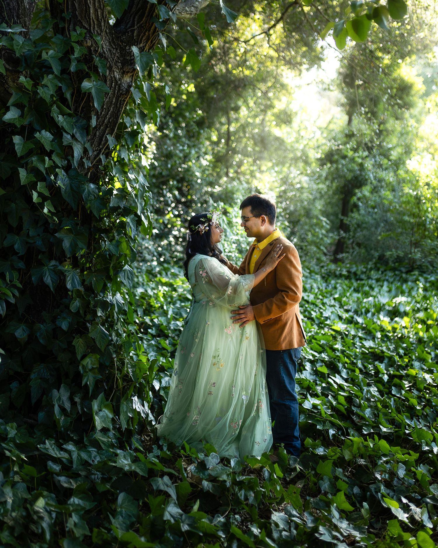 A romantic couple shares an intimate moment among lush green foliage in a garden setting.