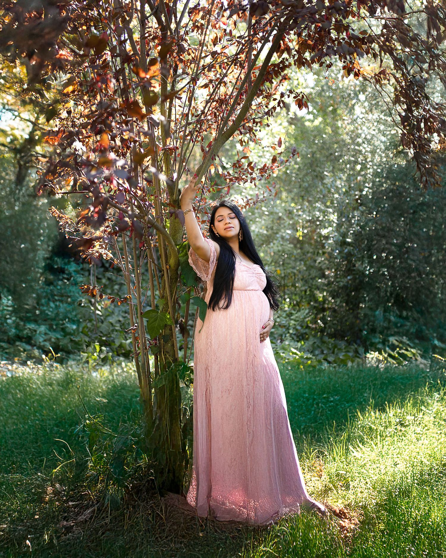 A person in a flowing pink tulle dress poses gracefully under autumn trees in a dreamy outdoor setting.