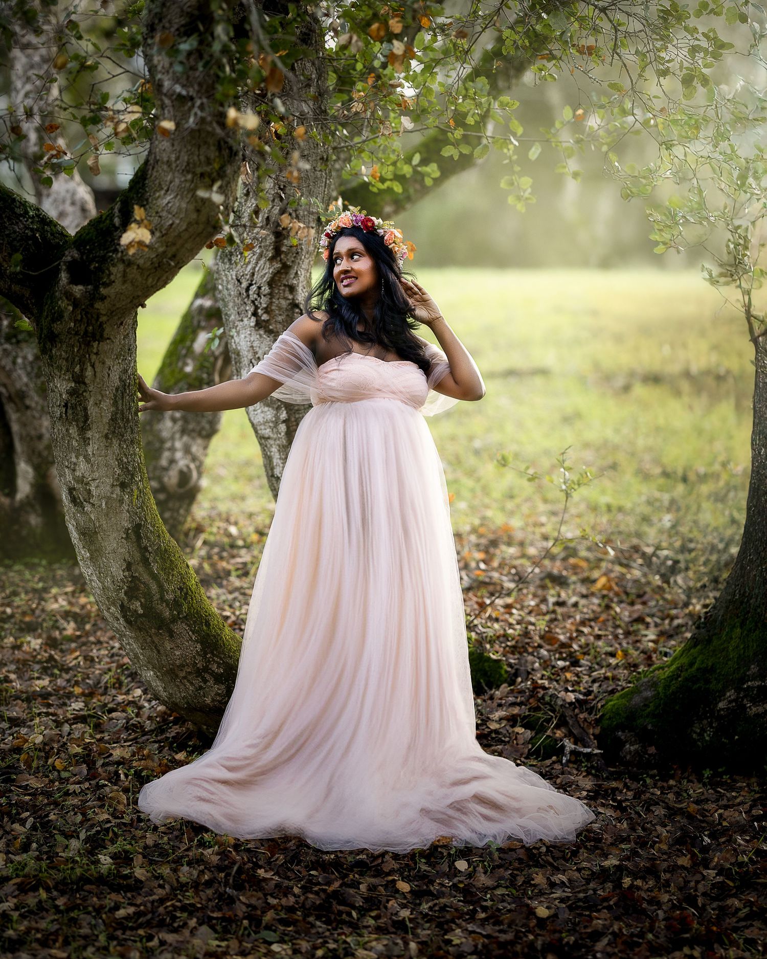 A dreamy outdoor photoshoot in a wooded setting with someone wearing a flowing pink tulle gown against autumn foliage.