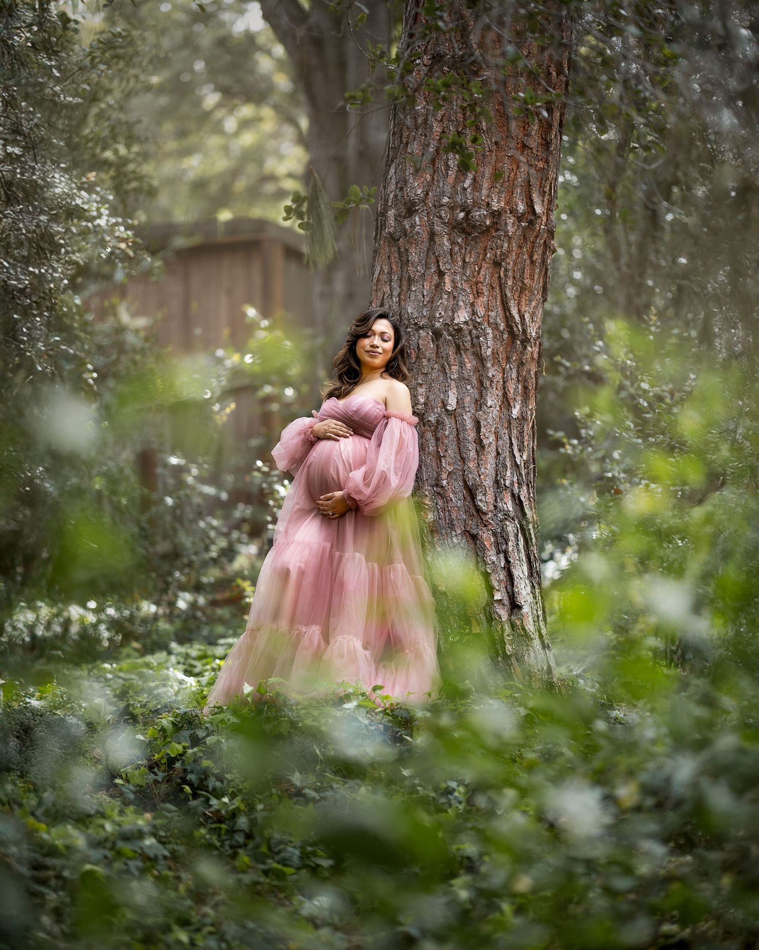 A dreamy portrait series in a forest setting shows someone in a flowing pink dress posing against a tall pine tree.