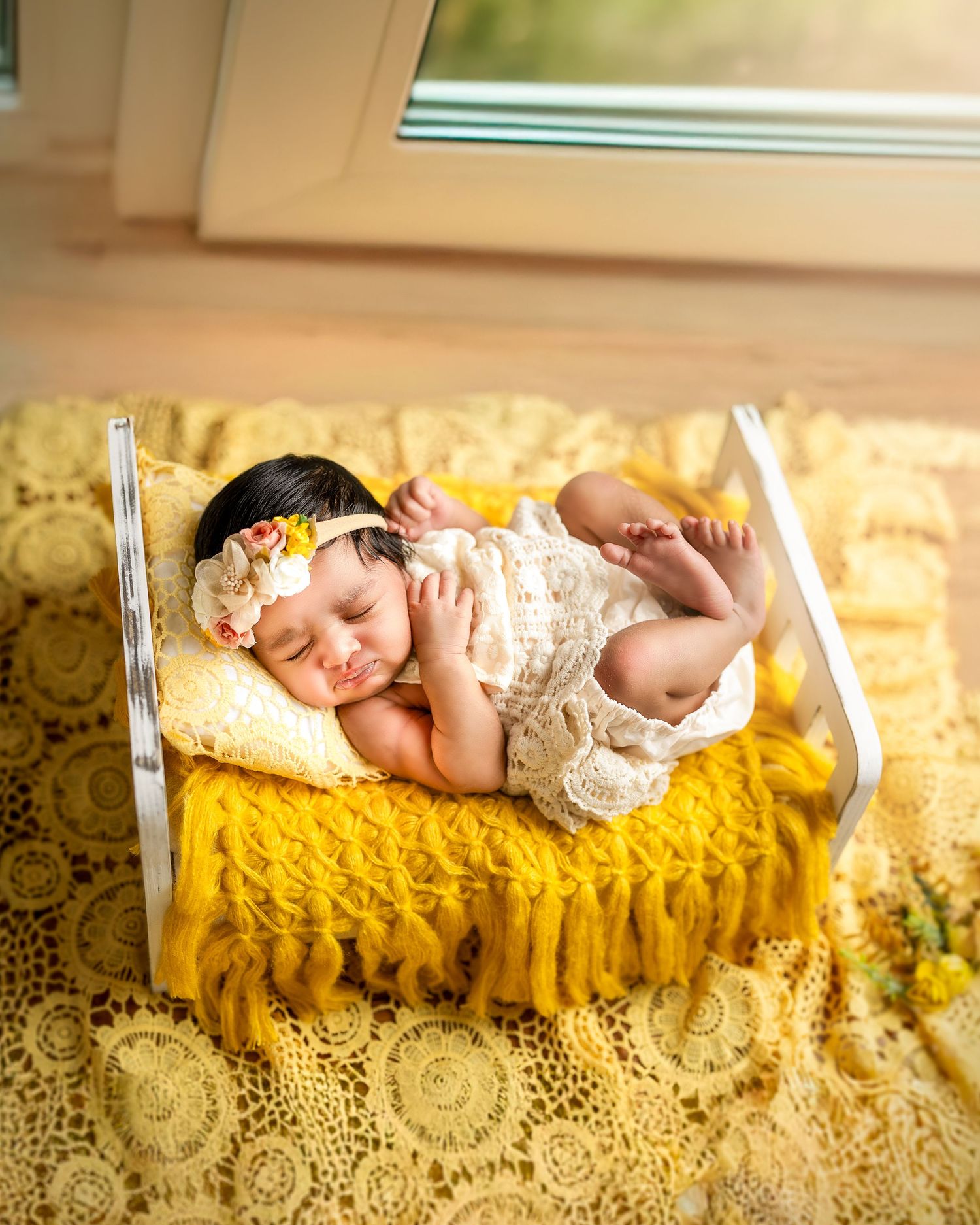 Newborn baby sleeping peacefully on a textured yellow blanket with lace details in warm natural lighting.