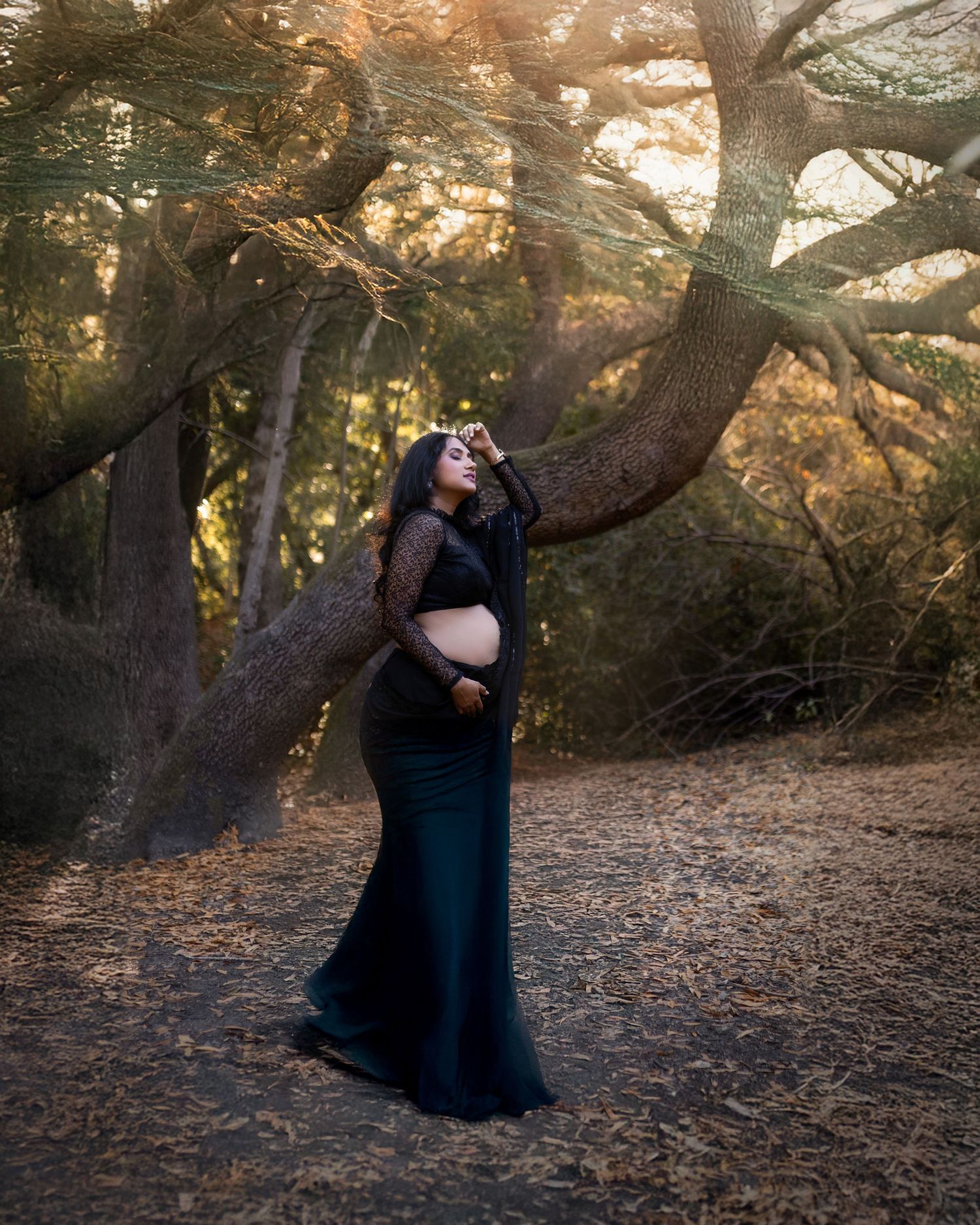 A silhouetted figure in a long dress stands among tall trees at sunset creating a dreamy forest atmosphere.