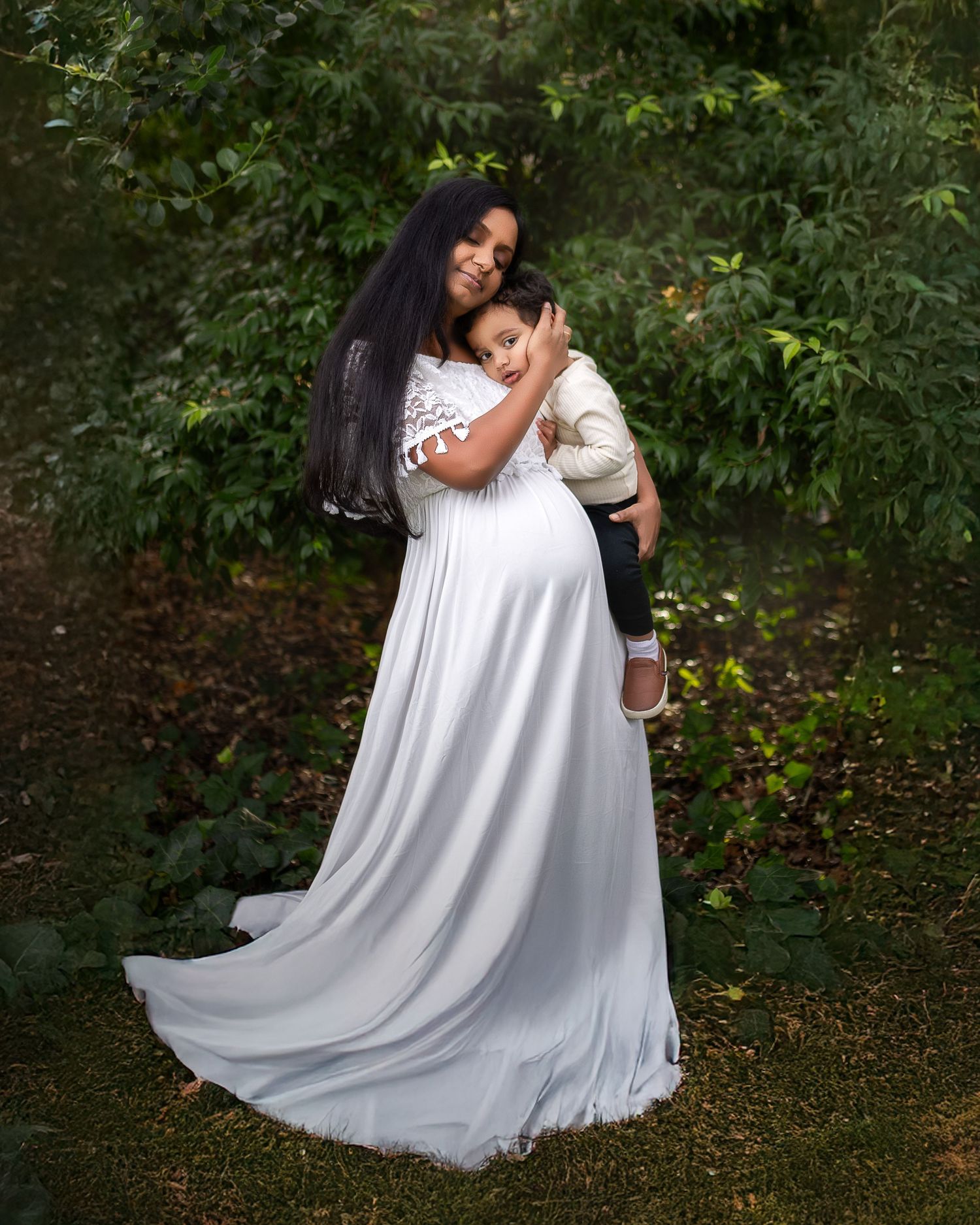 A person in a flowing white wedding dress stands in a garden setting surrounded by green foliage.