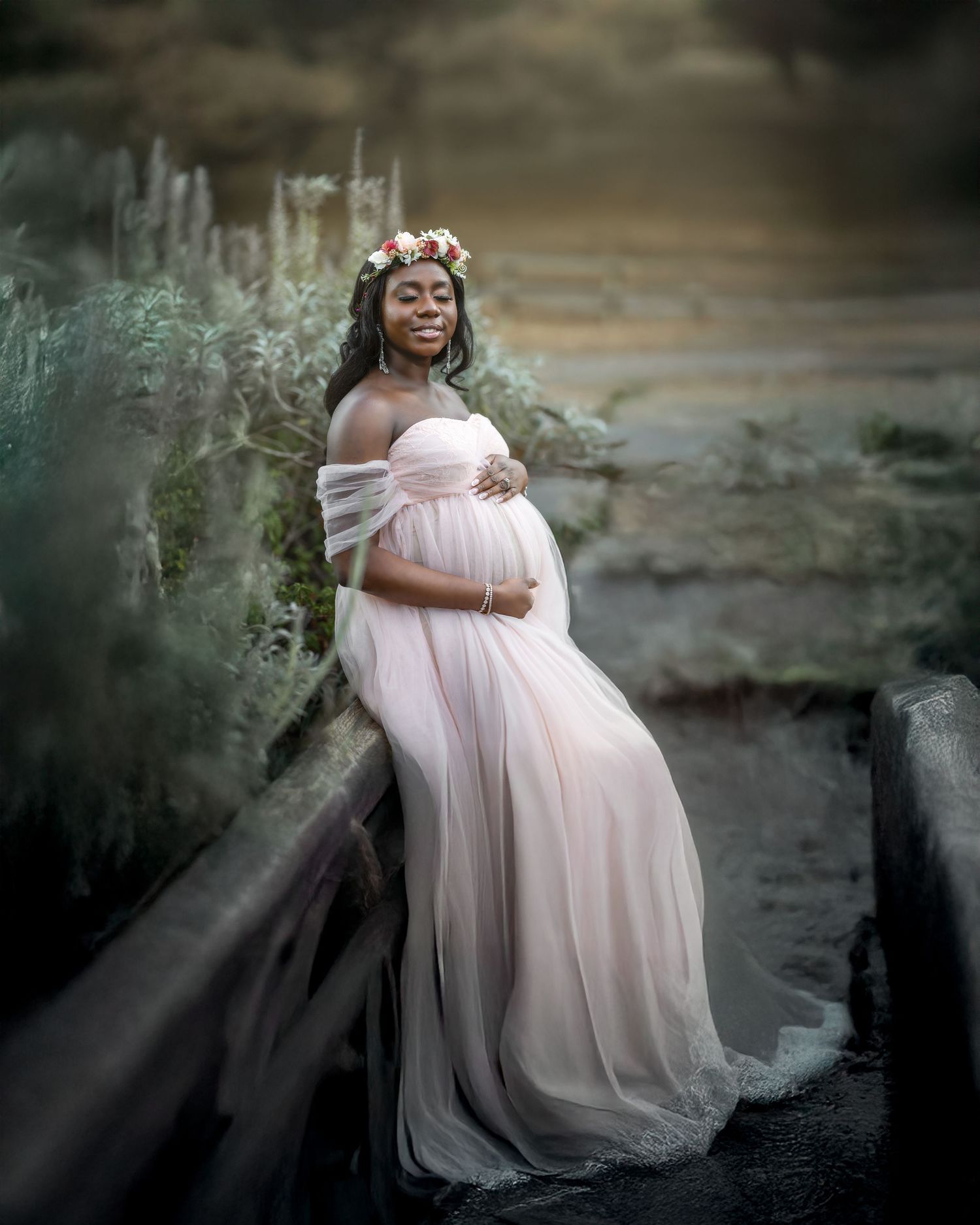 A person in a flowing pink tulle gown poses gracefully against a moody outdoor backdrop in a maternity photoshoot.