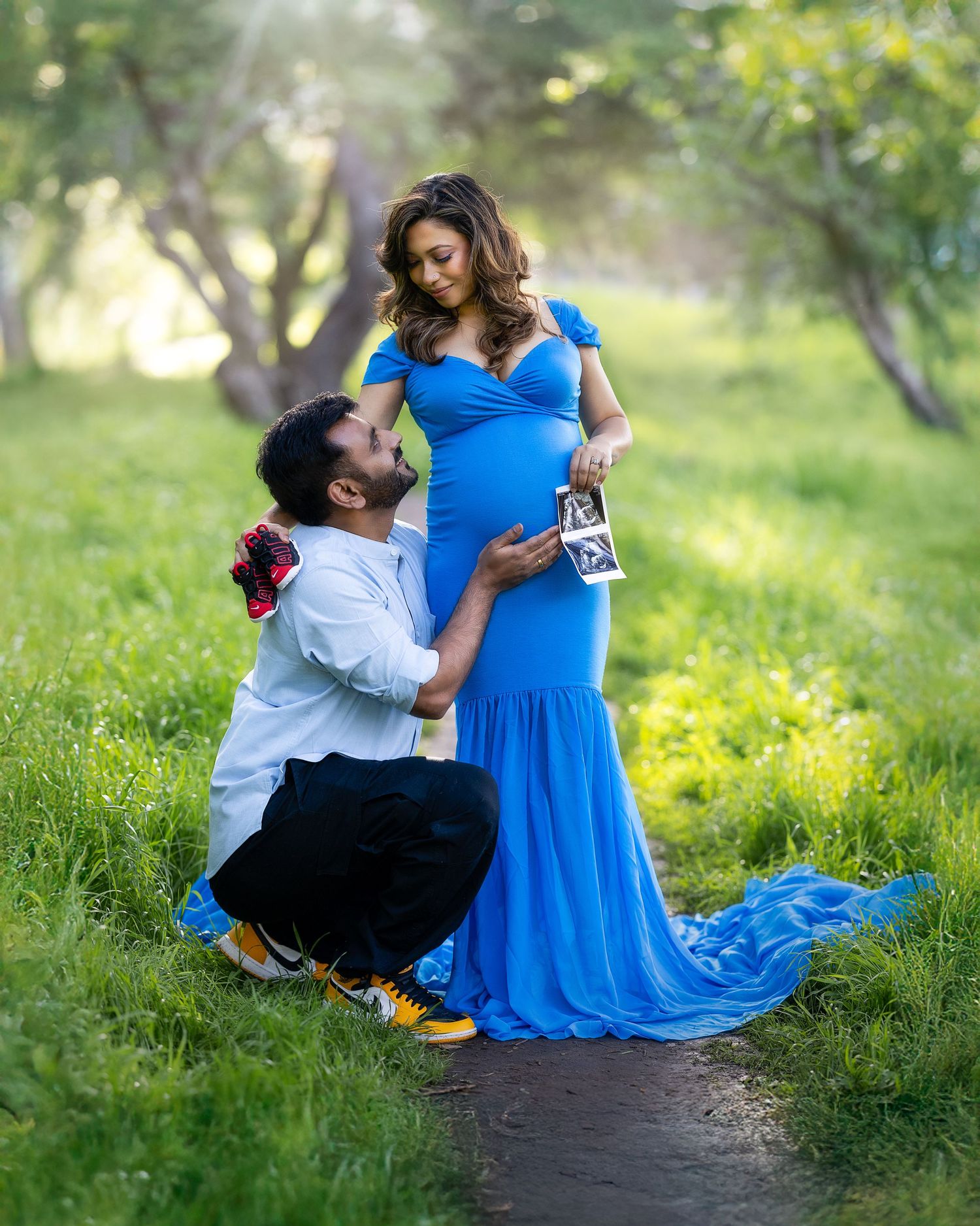 A couple in a blue dress and white shirt share romantic moments in a sunlit spring meadow with yellow wildflowers.