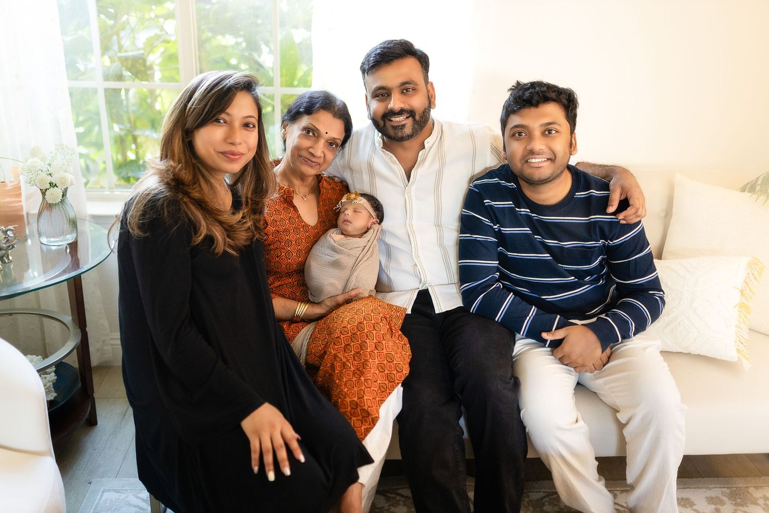 A group of people sitting together on a white couch and smiling warmly at the camera.