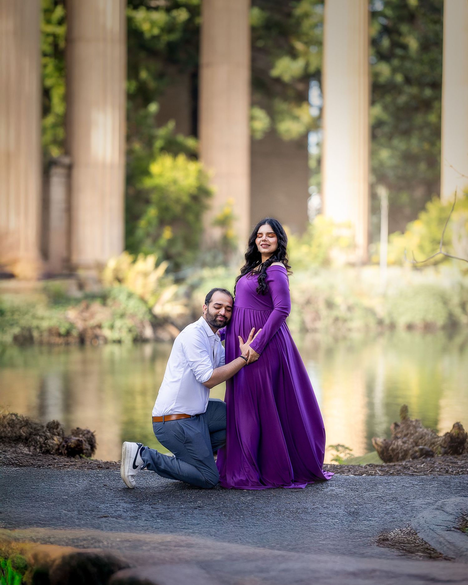 A romantic moment captured by columns and a pond as a couple poses in a purple gown and casual attire.