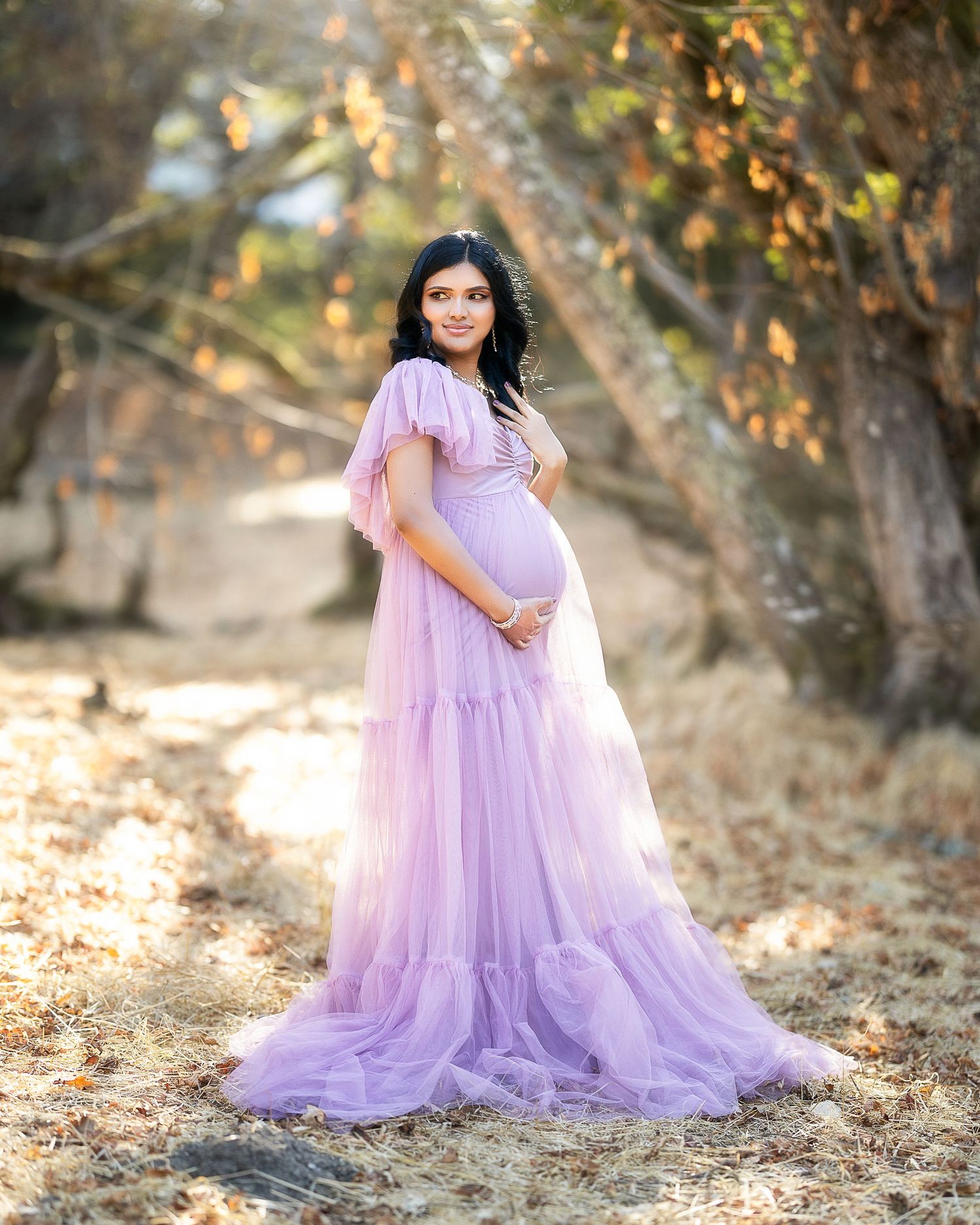 A flowing lavender tulle gown creates an ethereal look in an autumn woodland setting with golden sunlight filtering through trees.