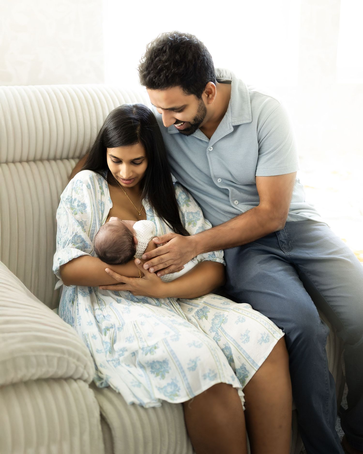 Parents sitting together on couch with newborn baby during intimate breastfeeding moment at home.