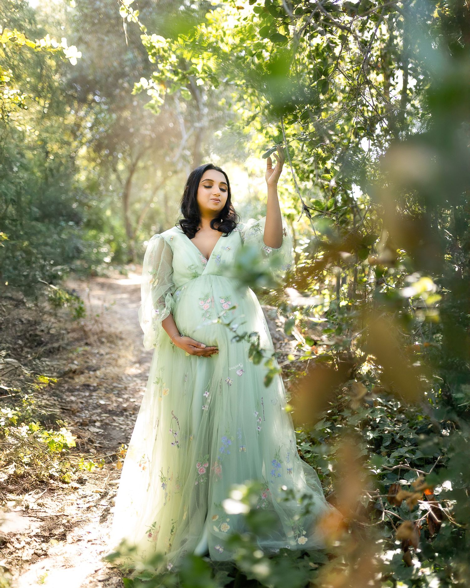 Two figures in ethereal mint green dresses pose gracefully among sunlit trees in a dreamy forest setting.
