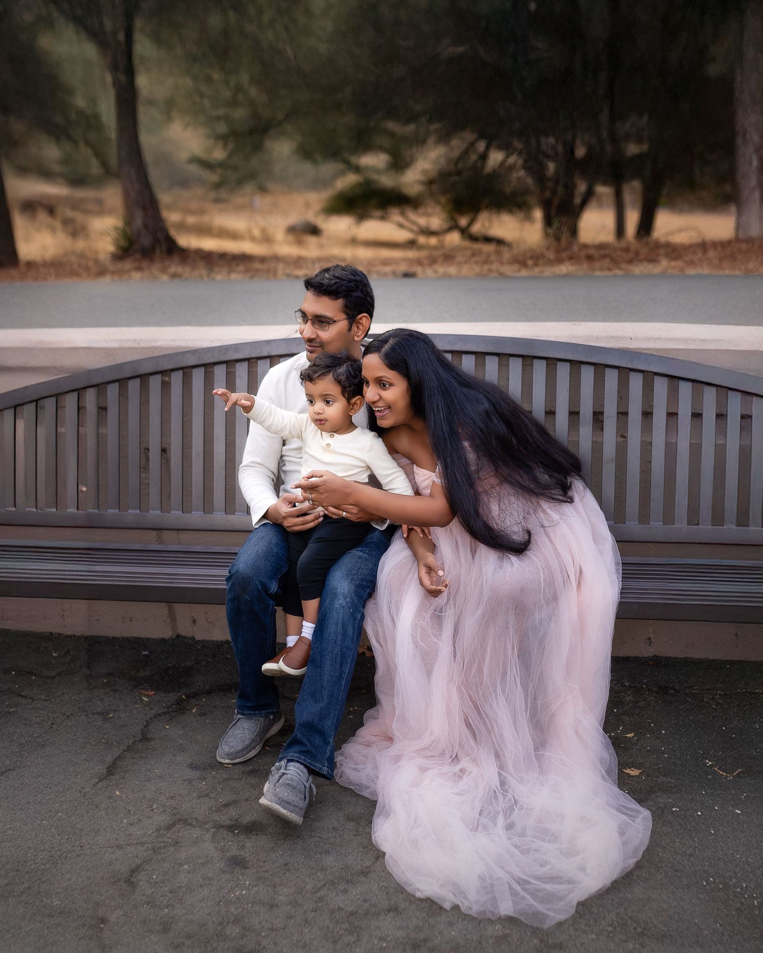A tender family moment captured on a wooden park bench as they share time together in matching soft pink and white outfits.