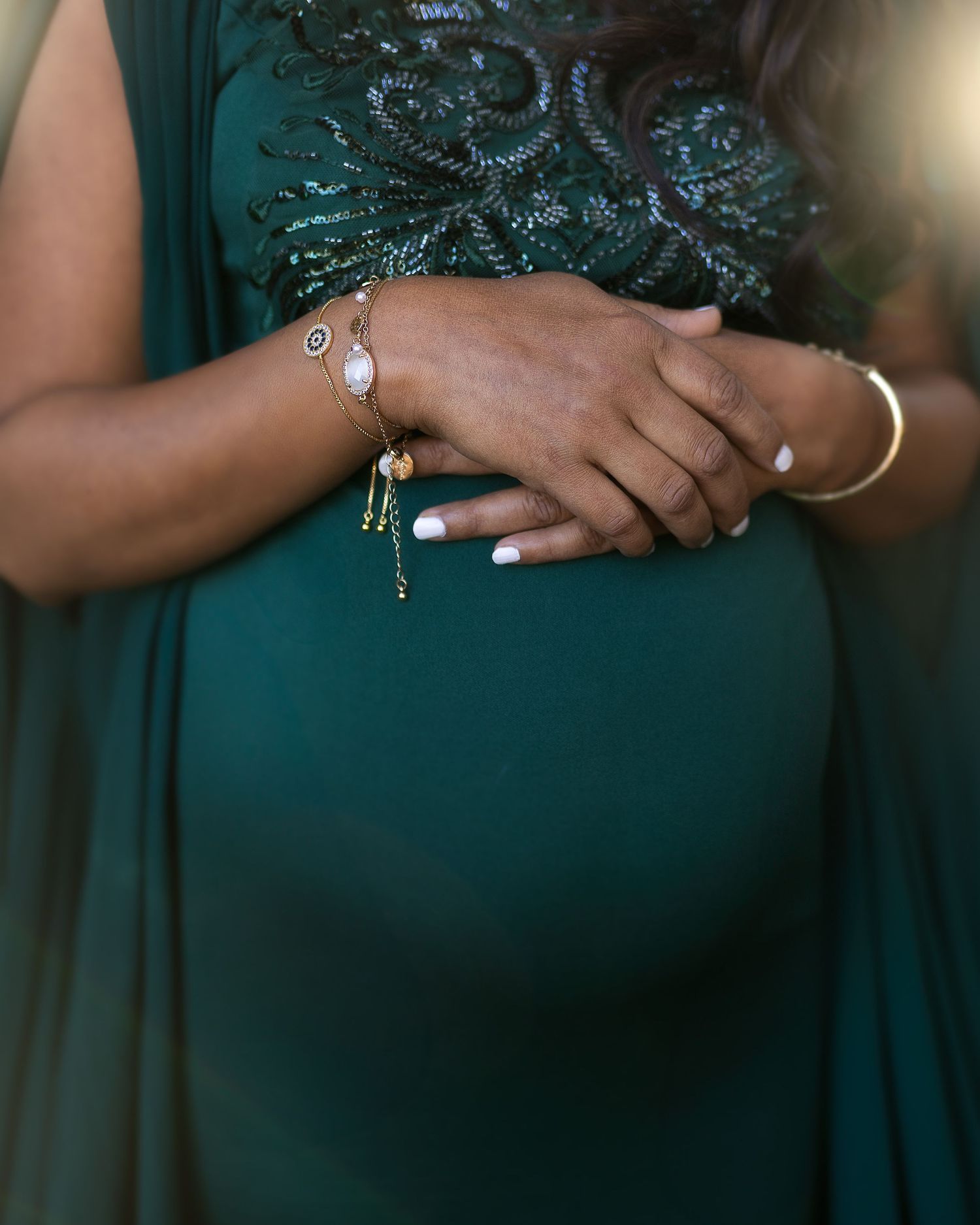 Close-up view of hands wearing jewelry and holding bouquets in emerald green formal attire.