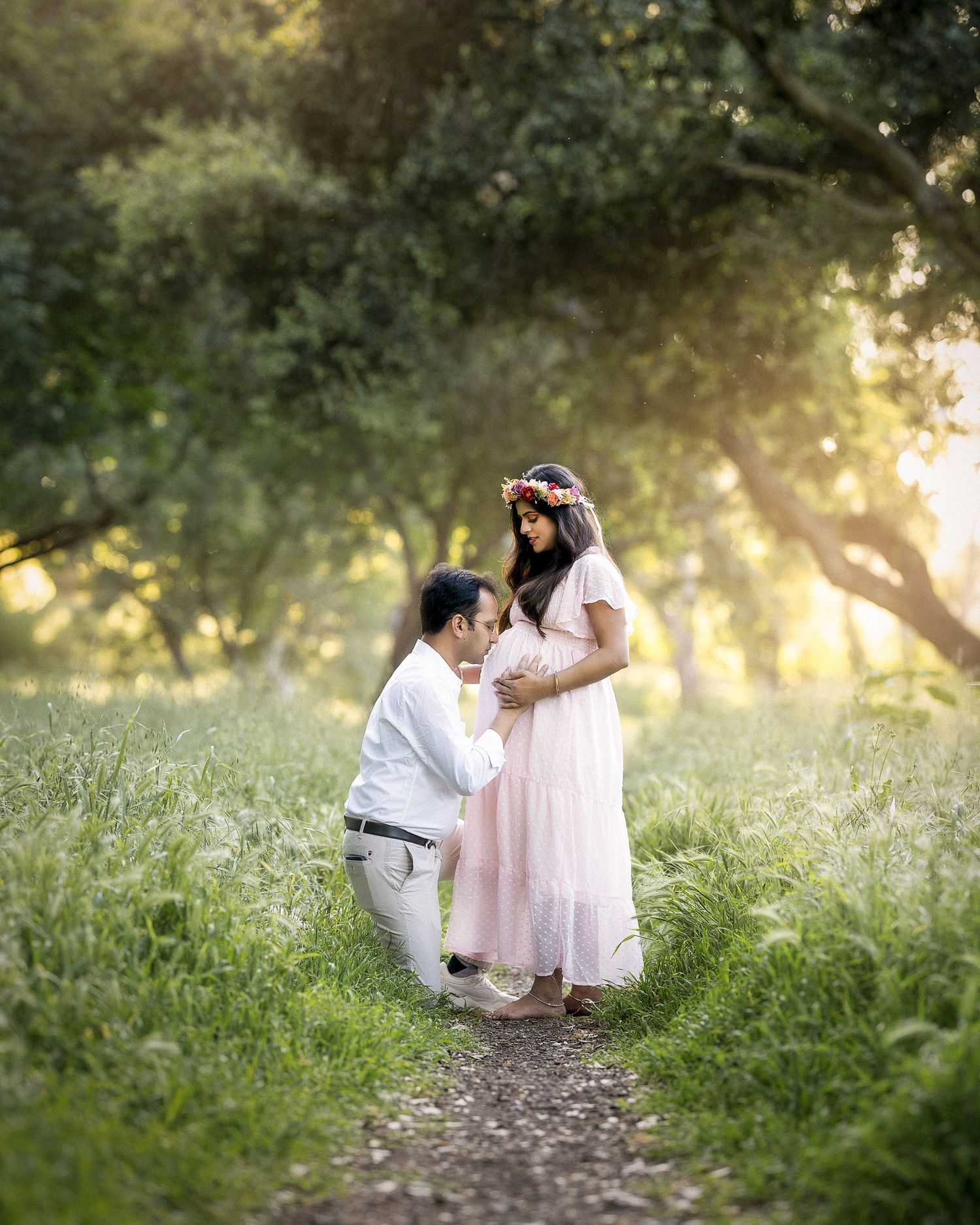 A child in a white dress sits in a dreamy garden setting while sunlight filters through trees in the background.
