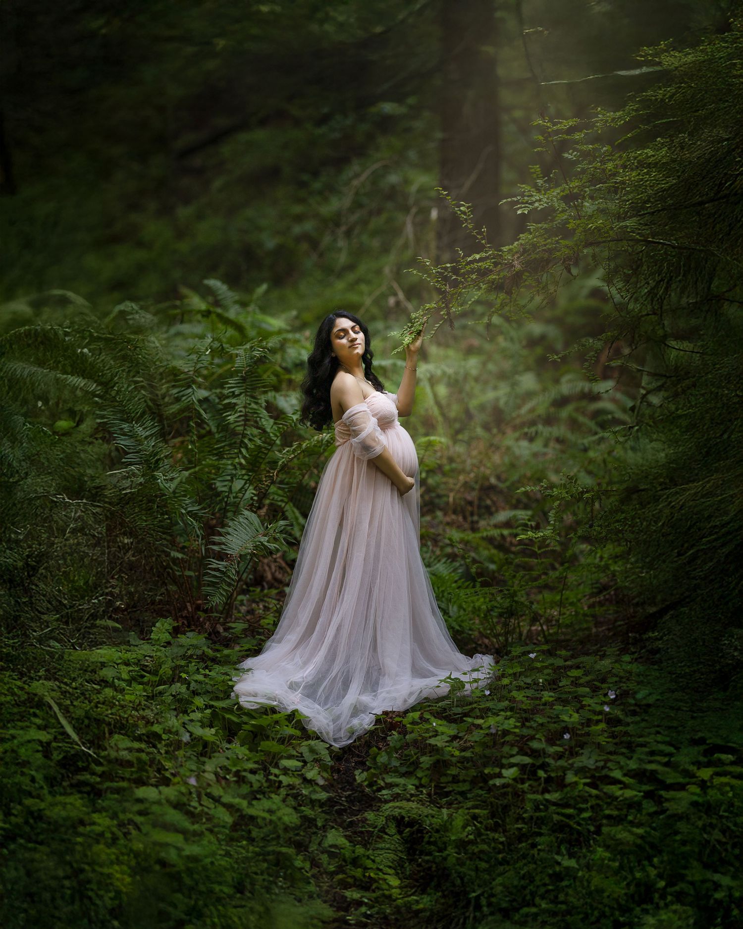 A figure in a flowing beige gown poses gracefully in a misty forest setting creating an ethereal woodland scene.