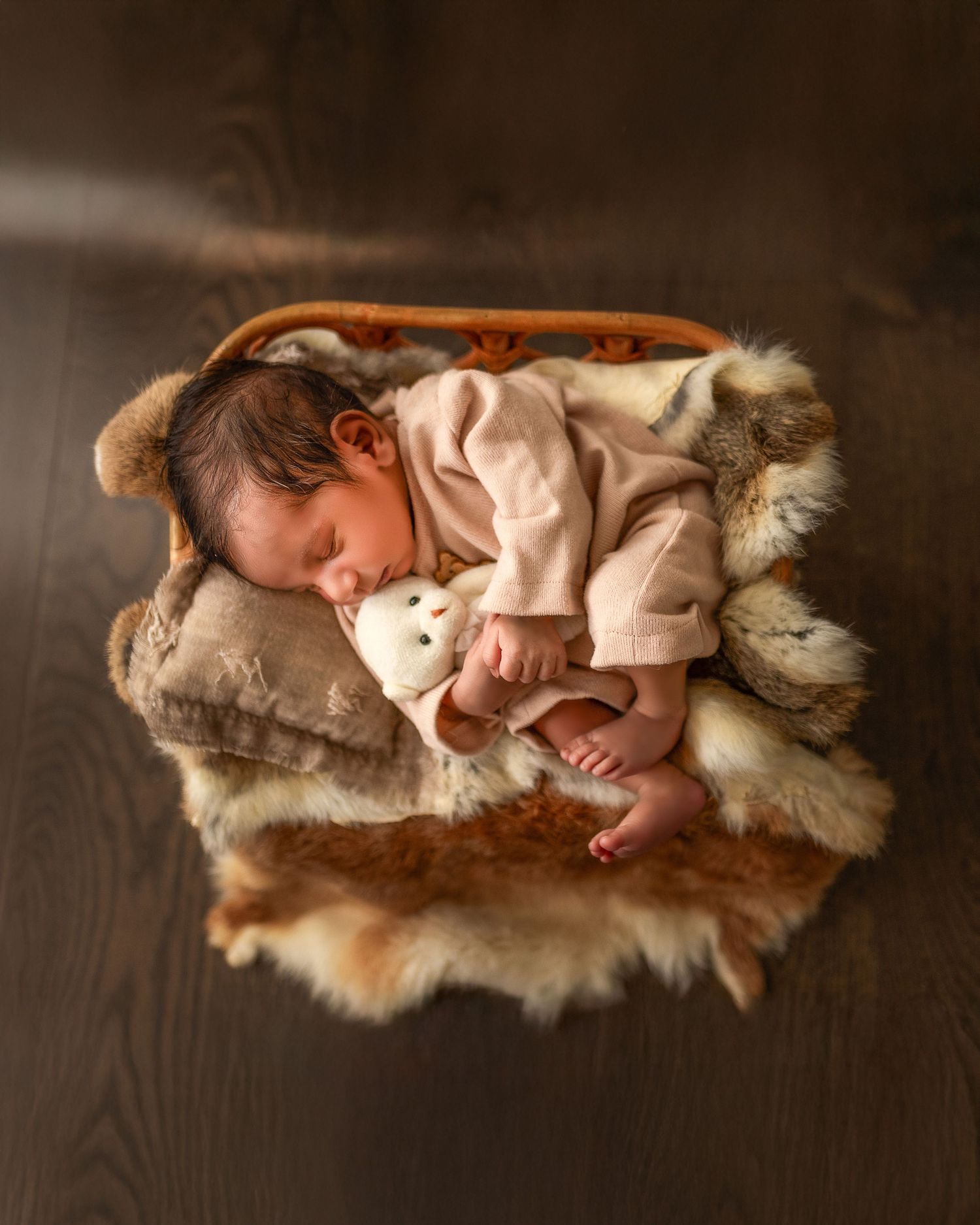 A peaceful sleeping baby in beige clothing rests on a cozy fur blanket in warm sepia tones.