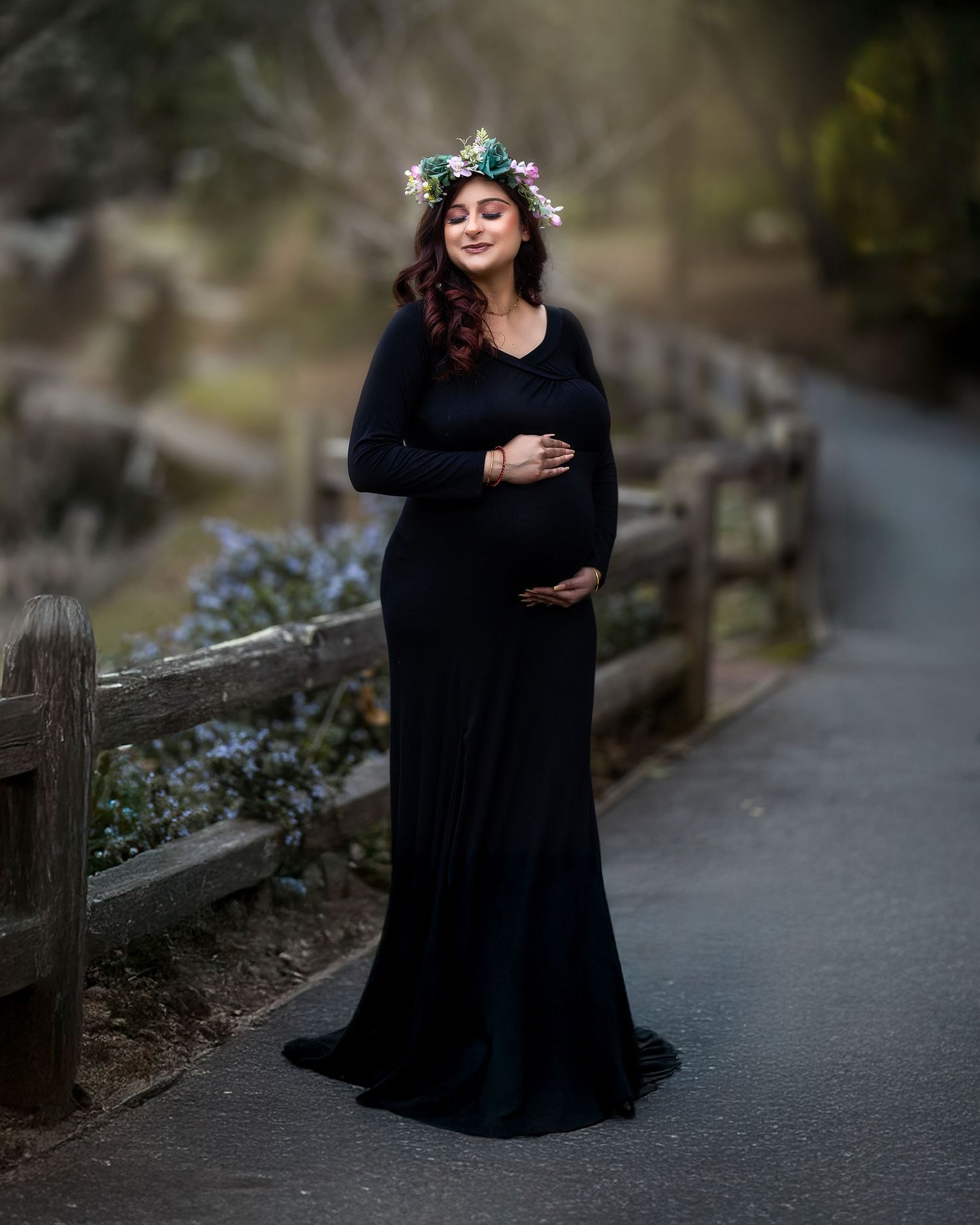 A person in a flowing black dress poses gracefully on a path surrounded by nature and flowers.