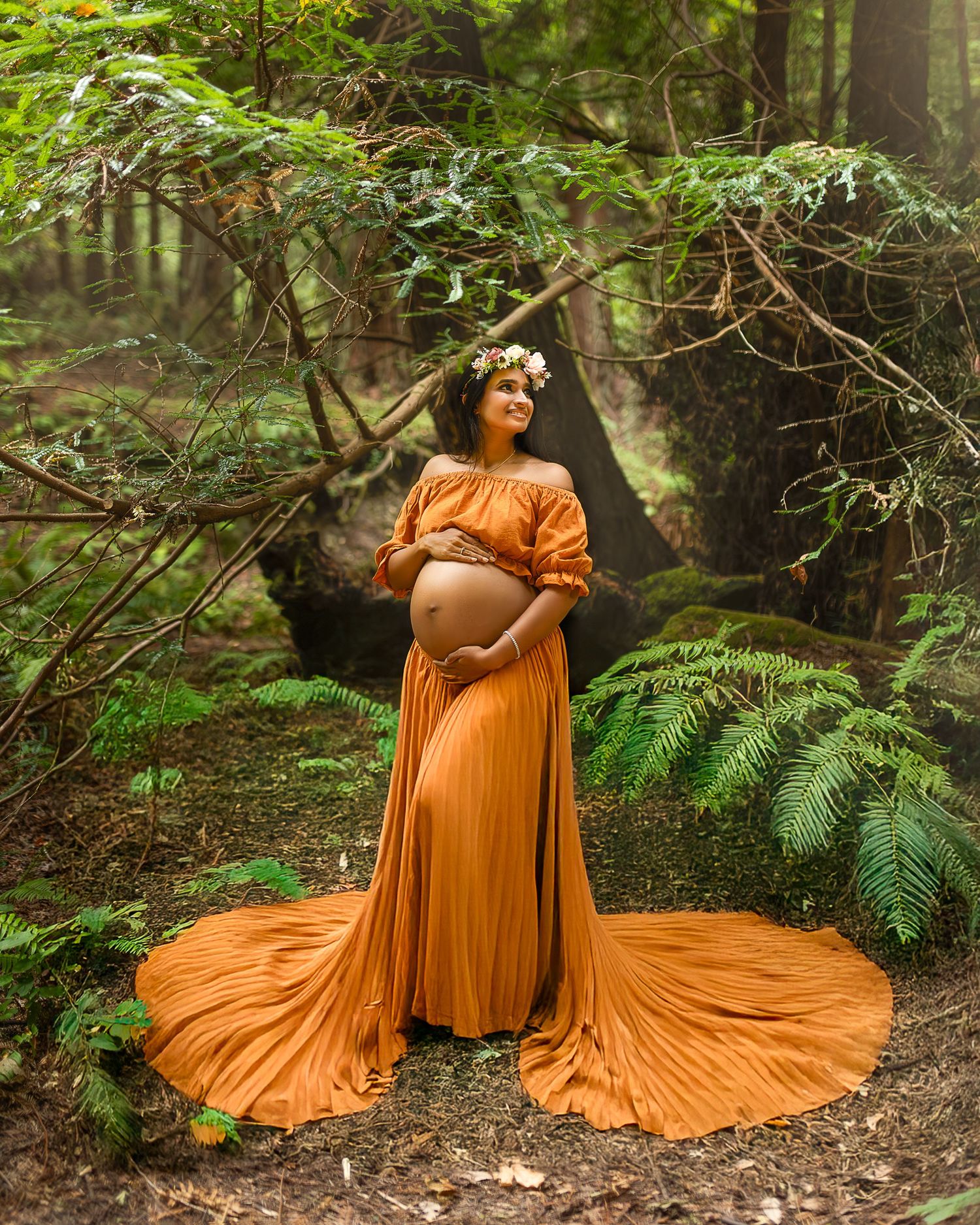 Person in flowing orange dress poses gracefully among ferns in a mystical forest setting.