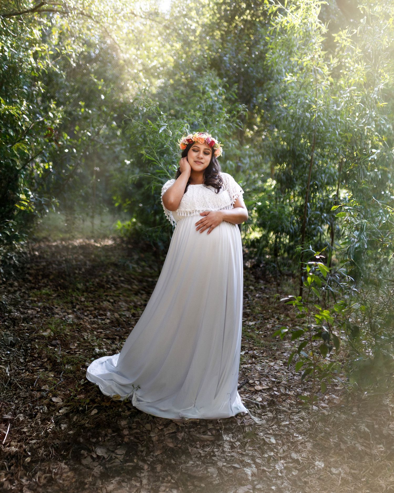 A person in a flowing white dress twirls gracefully in a sunlit wooded area creating an ethereal outdoor scene.