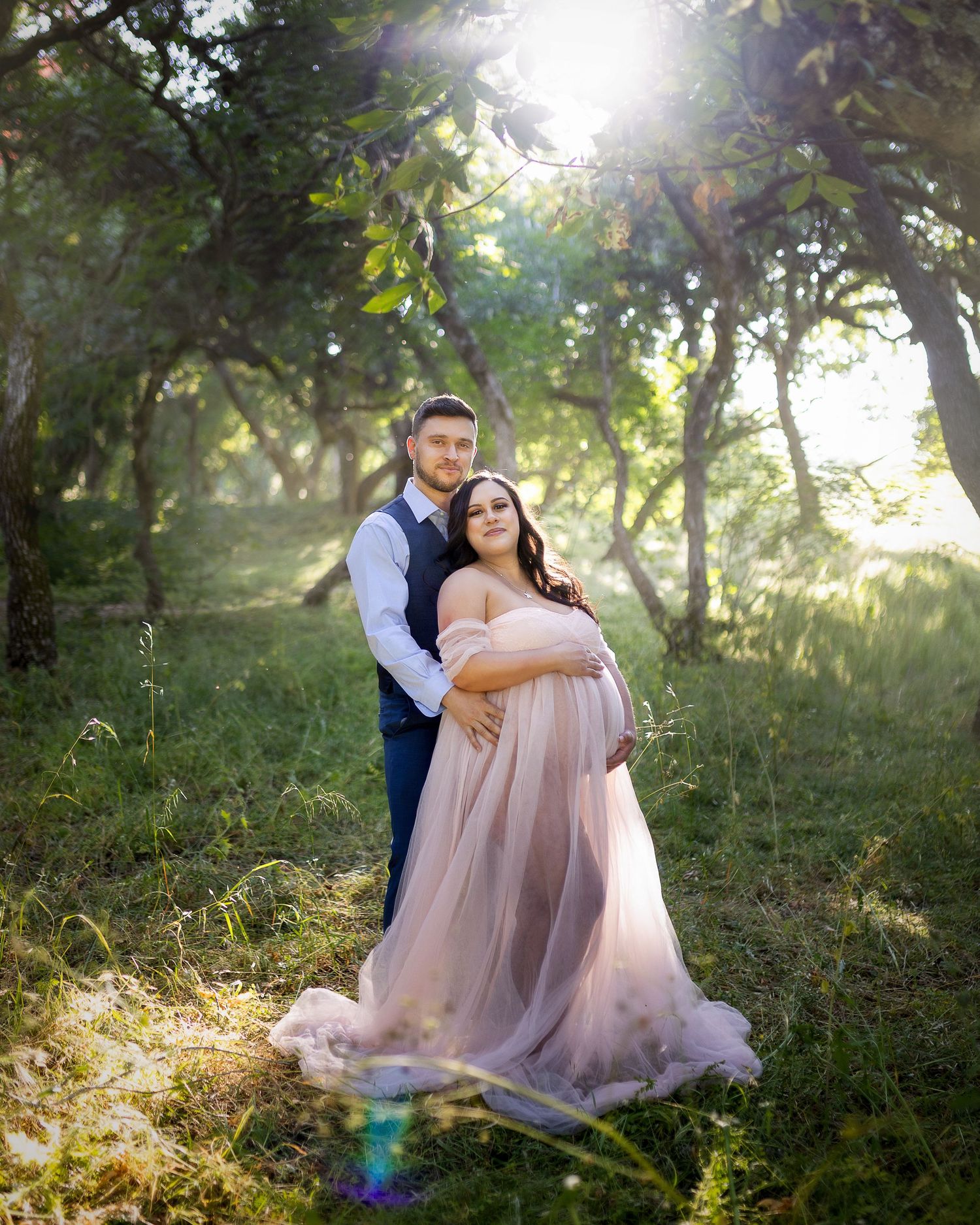 Romantic couple shares tender moments in a sun-dappled woodland setting with soft pink tulle dress.